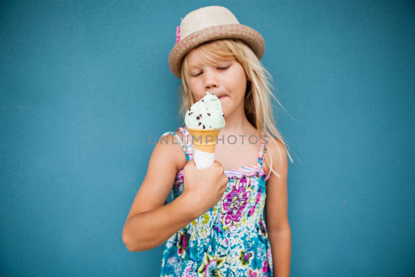 Cute young girl holding vanilla ice cream cone outside against blue wall background
