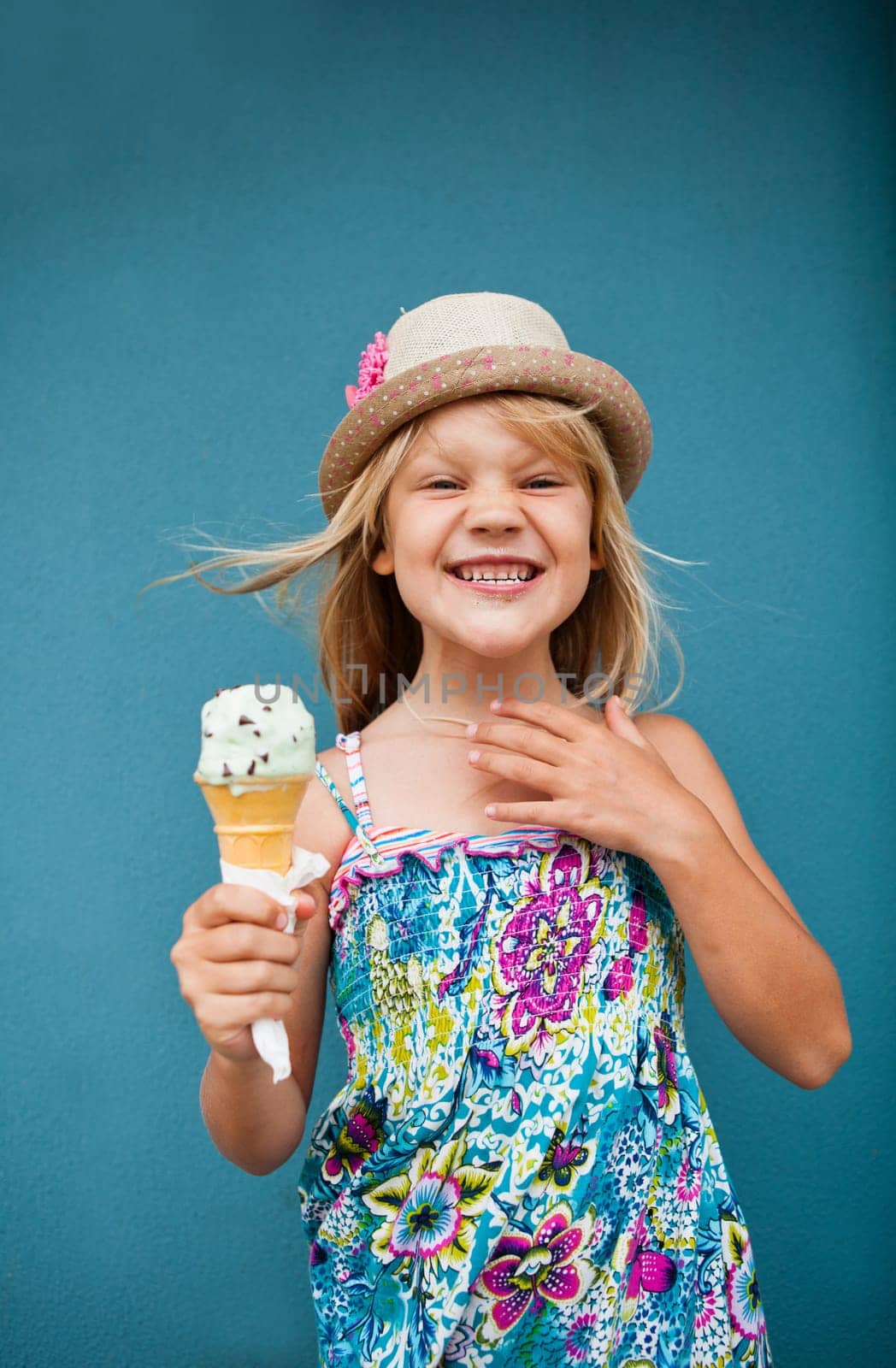 Cute smiling young girl holding ice cream cone outside against blue wall background