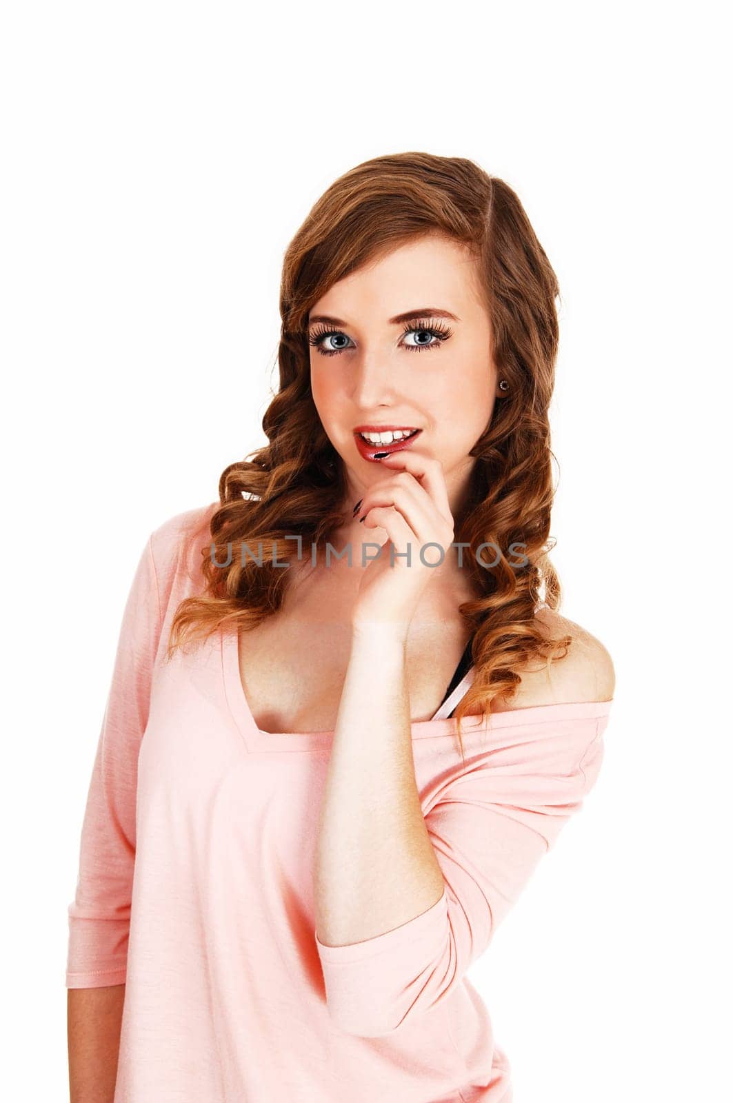 A beautiful young woman in a pink top and long curly hair standing for.white background with her hand on her chin..