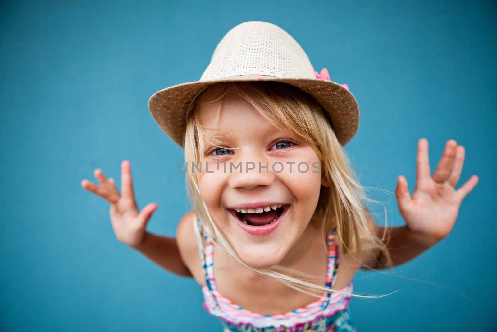 Portrait of stylish cute young girl being playful outside against blue wall background with focus on face