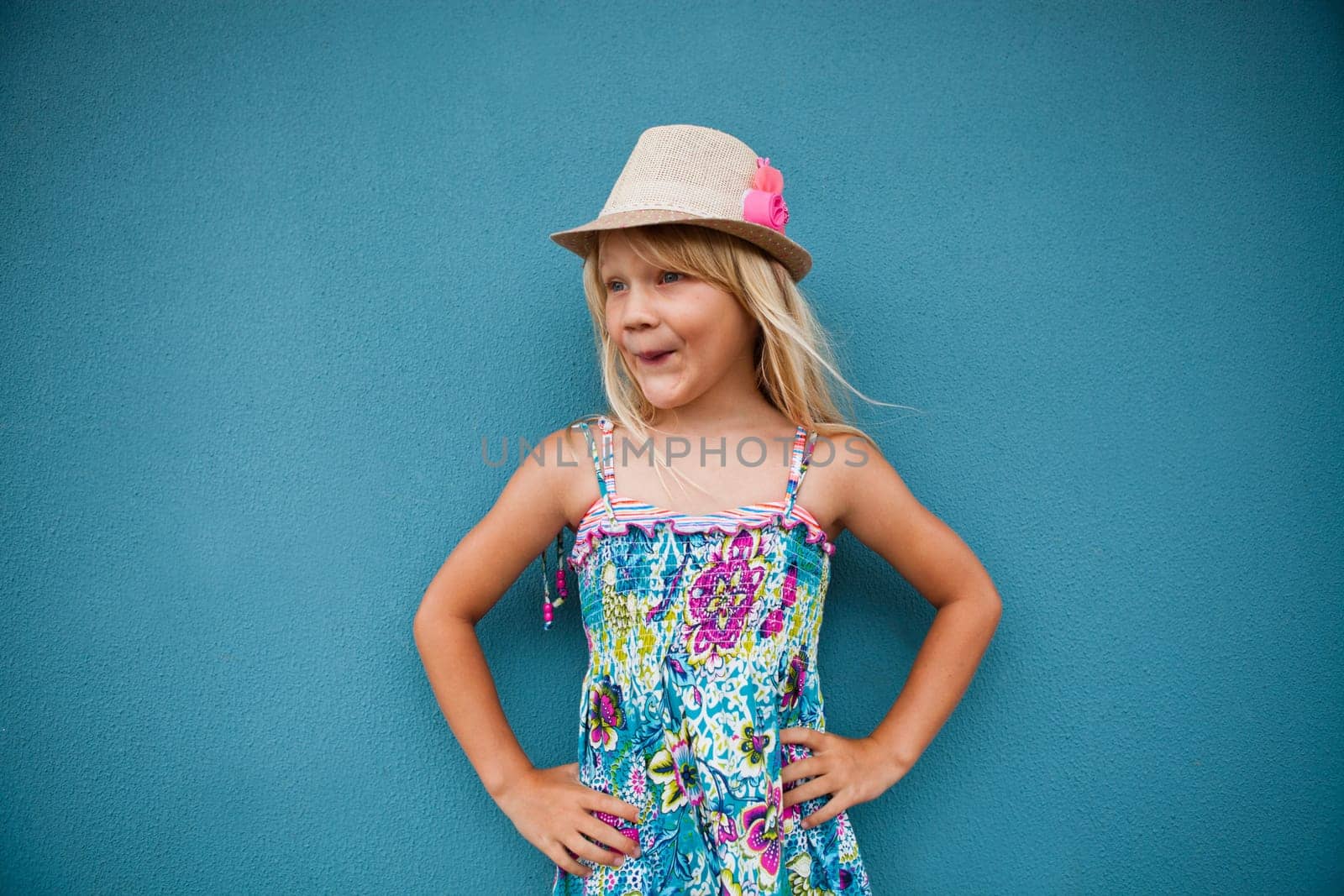 Portrait of stylish cute young girl with funny expression outside against blue wall background