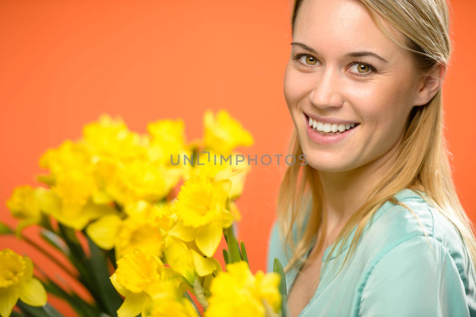 Smiling woman with spring yellow narcissus flowers on orange background