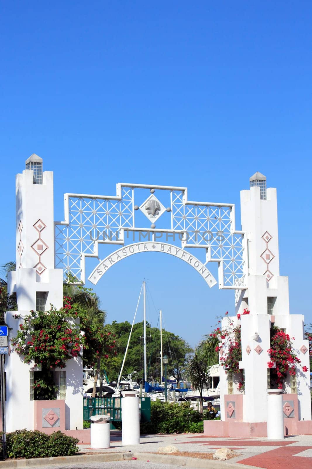 SARASOTA, FLORIDA - MAY 9, 2013: Beautiful entrance to Sarasota Bayfront, opened in 1992, that has red flowers and surrounded by tropical foliage and trees with people and boats in the background.