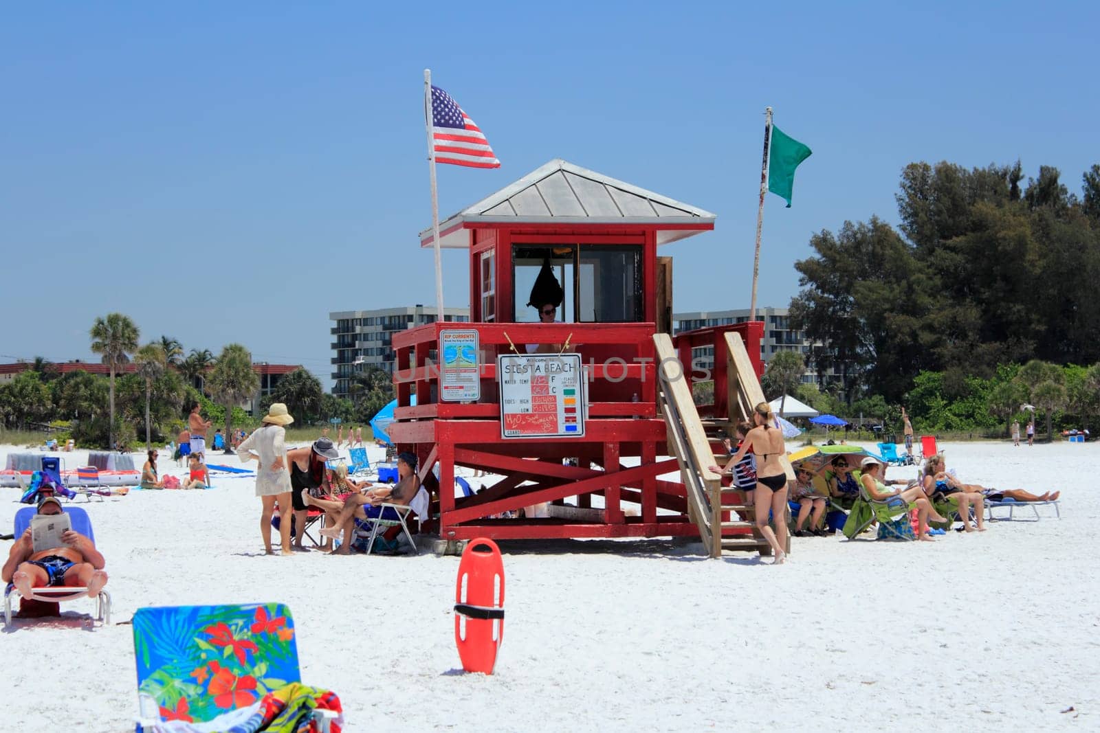 SIESTA KEY, FLORIDA - MAY 9, 2013: Red lifeguard tower flying green and American flags with a lifeguard present and lots of people around relaxing at  beautiful Siesta Beach on a very sunny, warm day