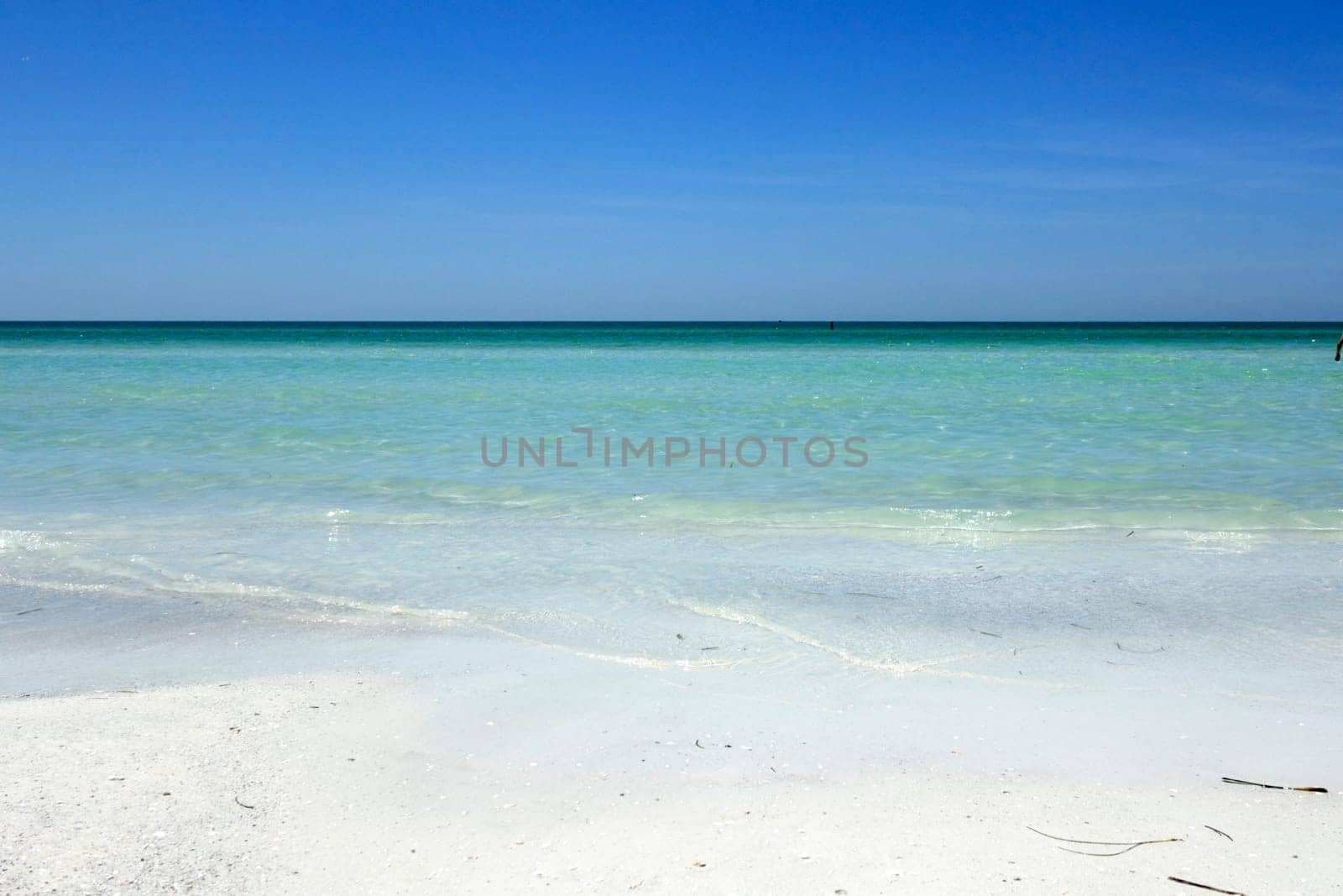Beautiful distant view of calm, clear Gulf coast turquoise tropical water and horizon seen from the white quartz sand shore of Siesta Beach under a sunny blue sky.