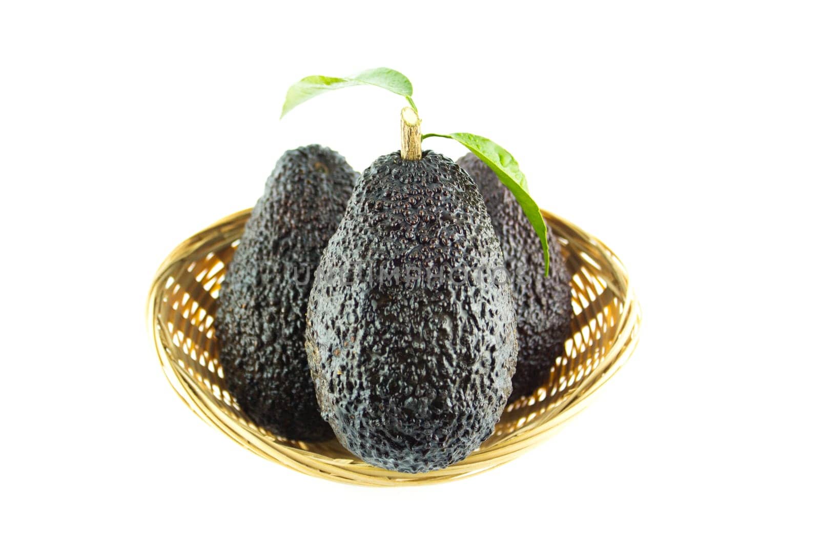 Avocados with leaves on a Dish of straw.