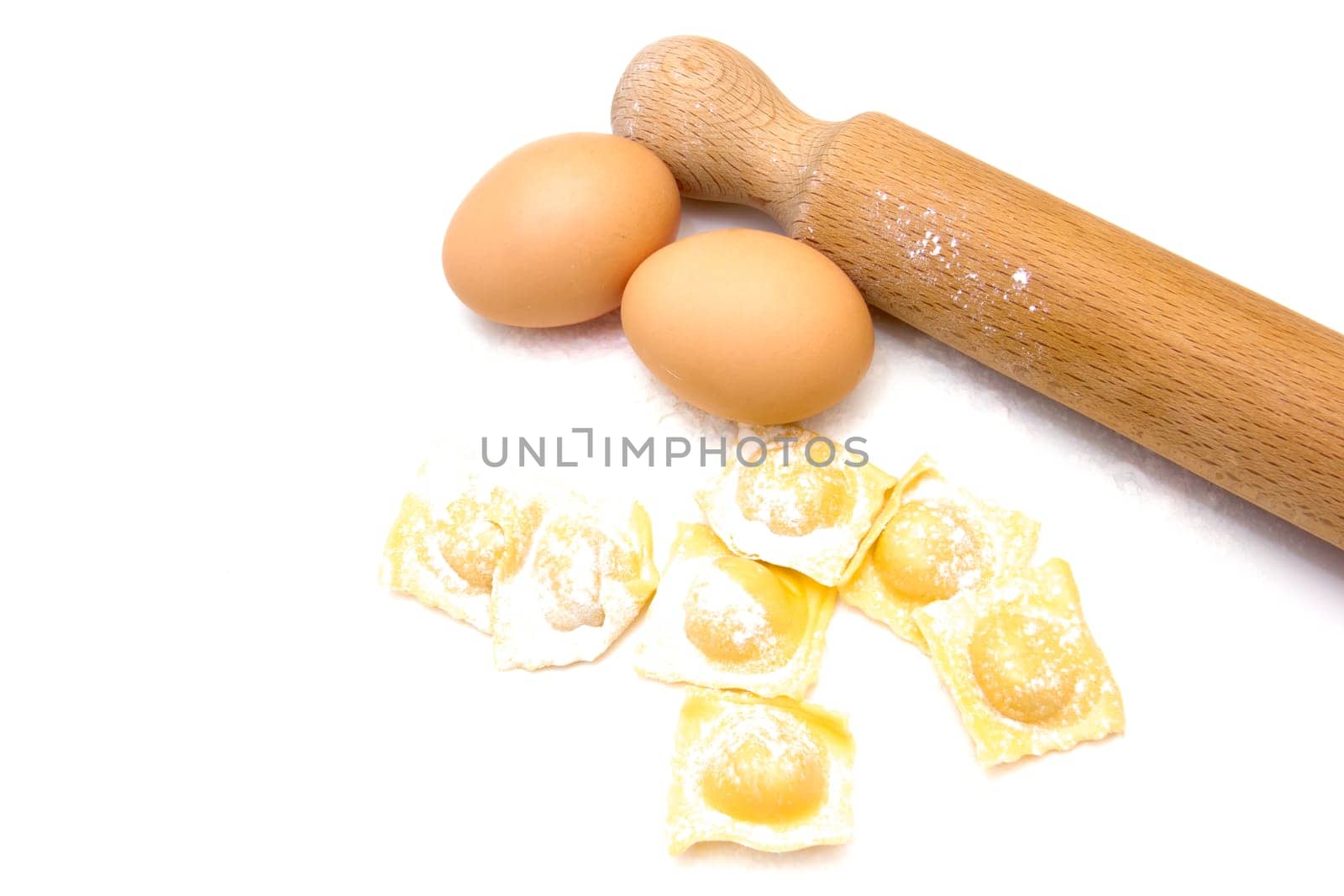 Ravioli with eggs and rolling pin on white background