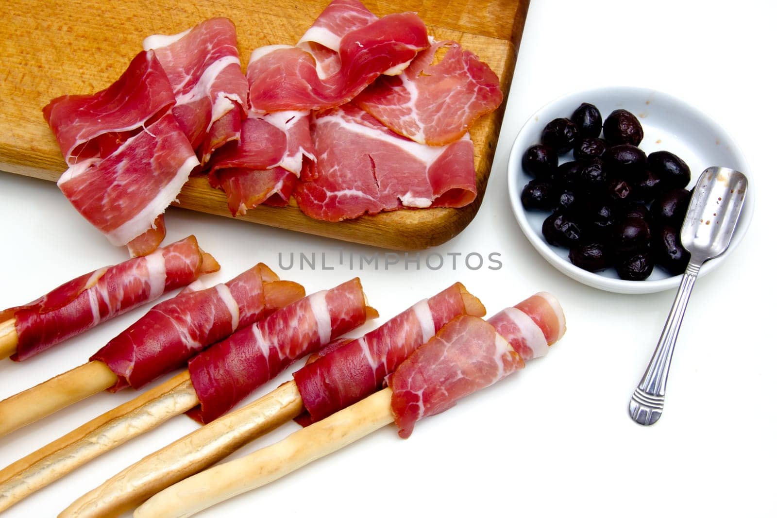 Slices of ham on cutting board and black olives on white background