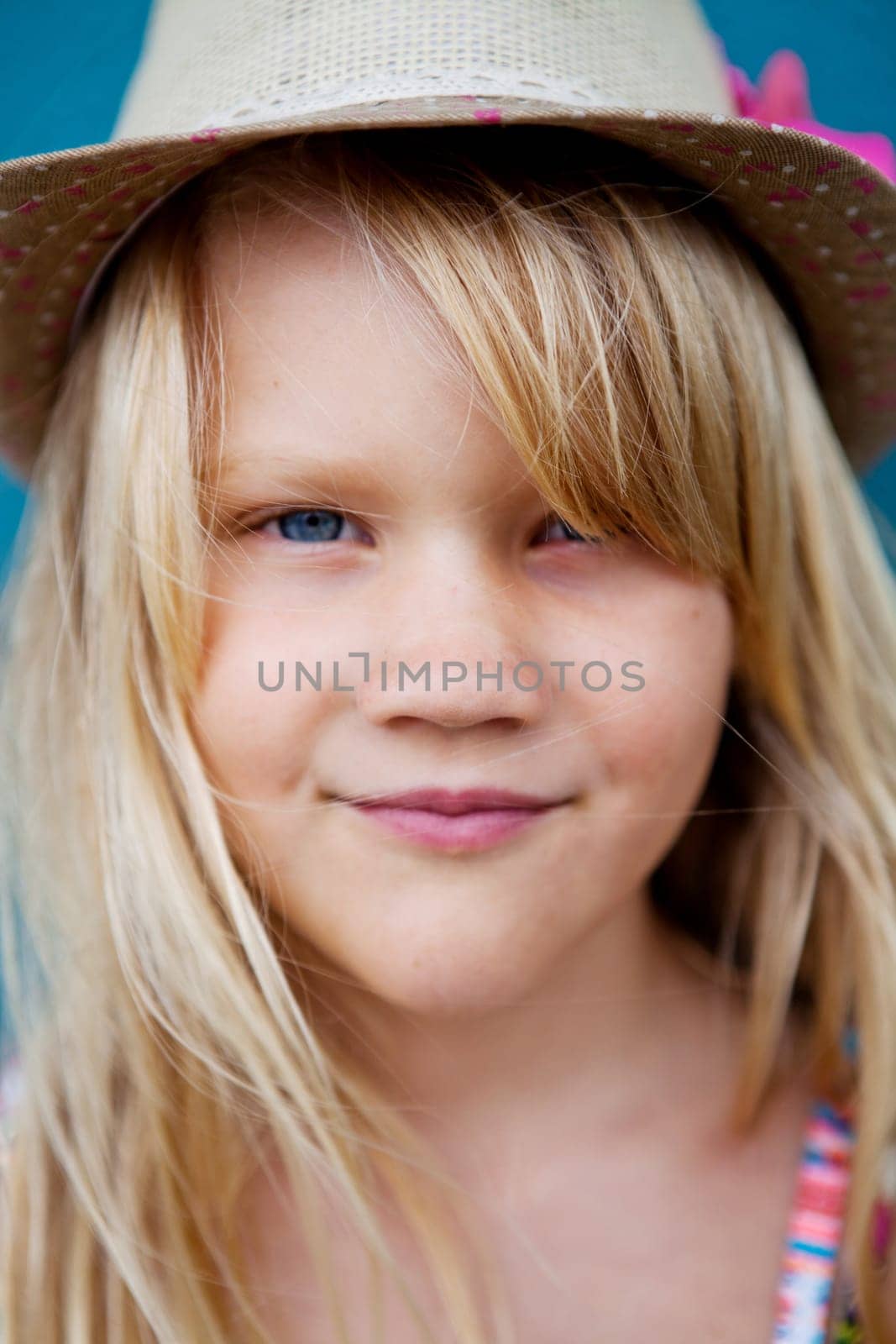 Closeup of face of cute smiling young girl with stylish hat outside against blue wall background