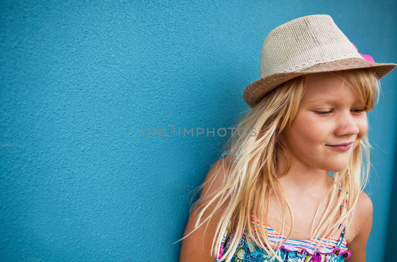 Cute young girl wearing stylish hat smiling outside against blue wall background
