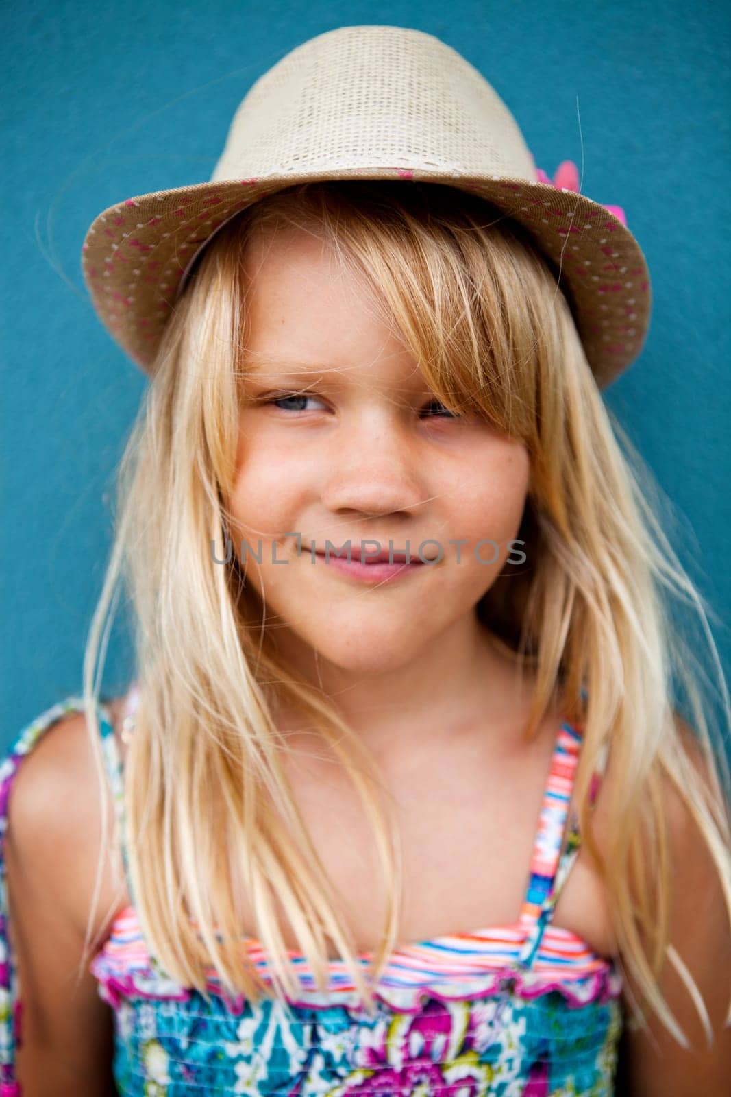Portrait of cute smiling young girl wearing stylish hat outside against blue wall background and looking to side