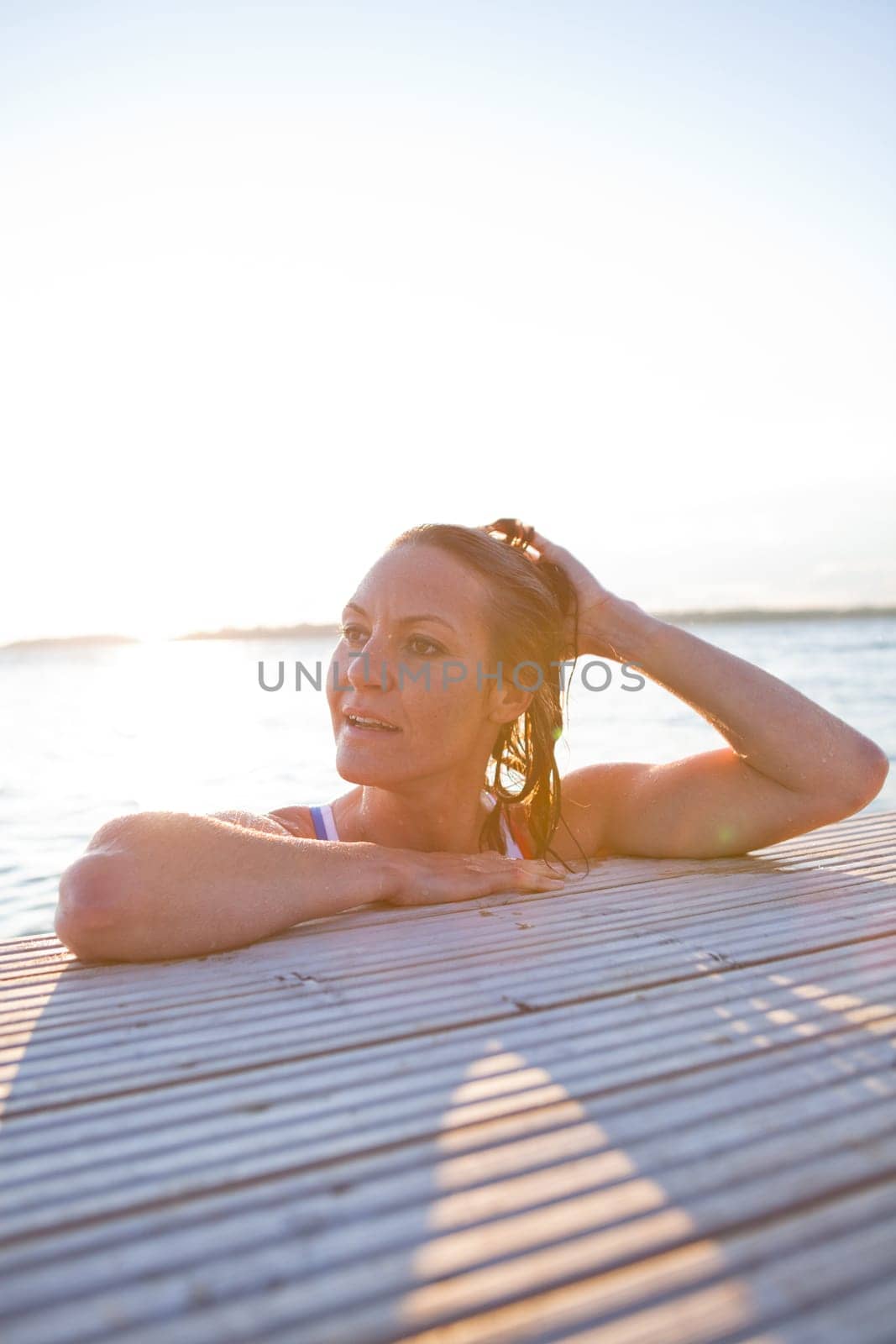Attractive woman in white bathing suit resting at edge of wooden pier in nordic country during summer