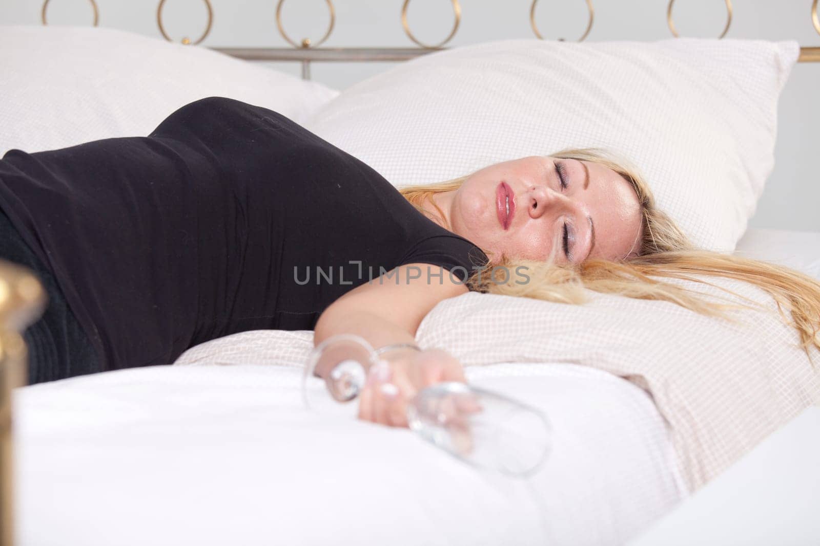 Drunk woman in black shirt with glass, sleeping in bed