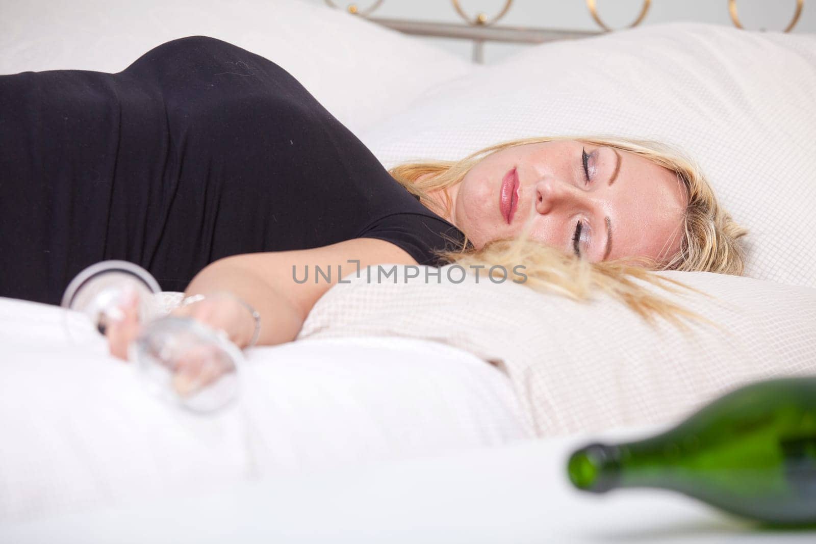 Drunk woman with glass, sleeping on bed
