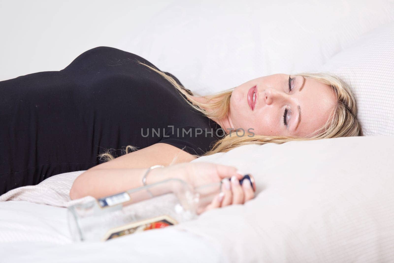 Drunk woman lying on bed, holding a bottle of alcohol