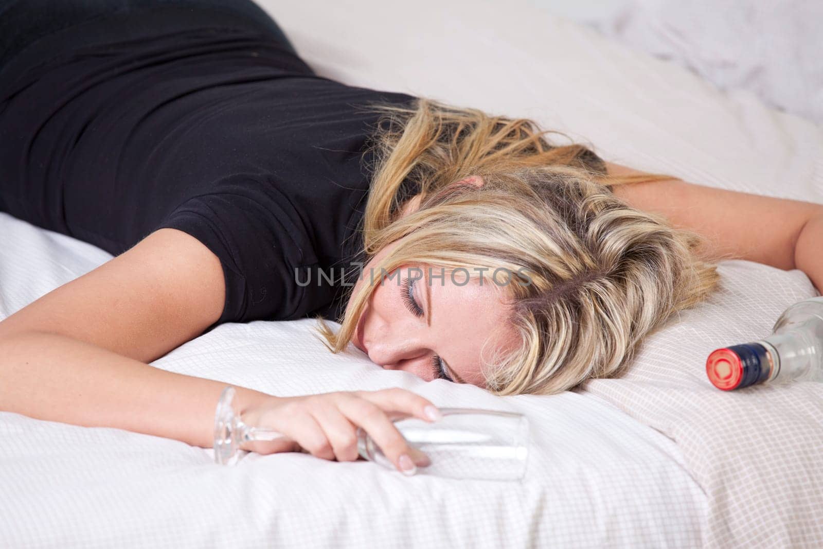 Drunk woman sleeping after party with glass and bottle of alcohol in bed