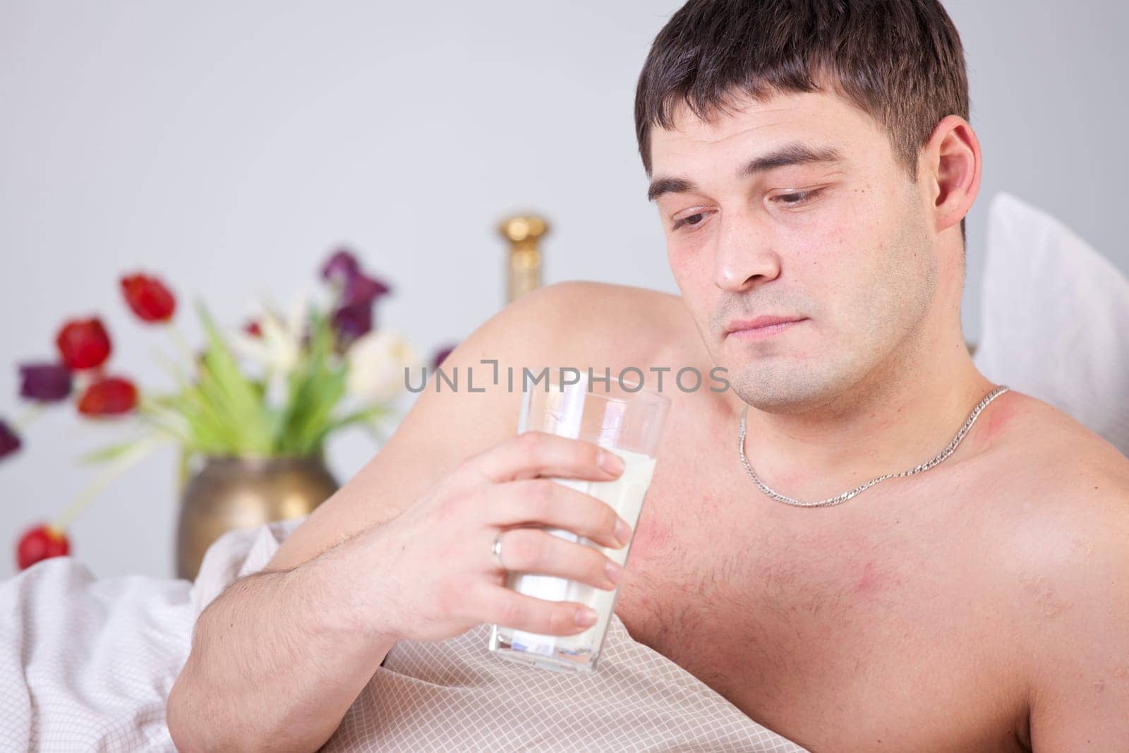 Sick and unhappy man with glass milk on bed