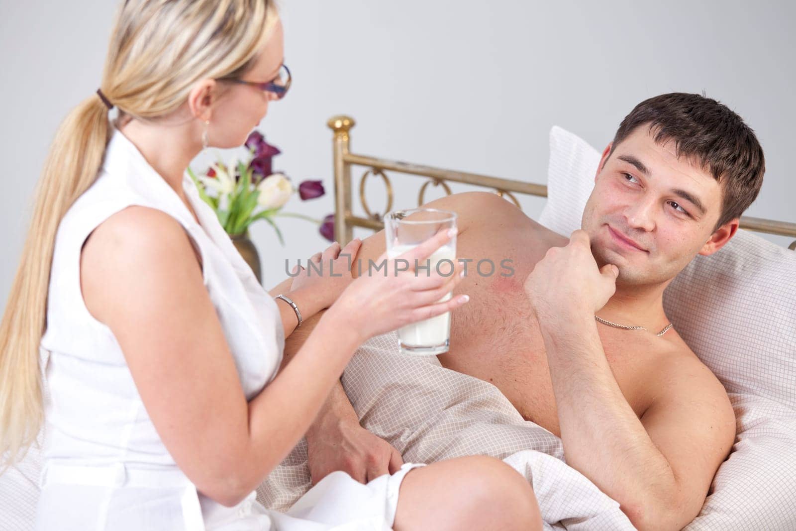 Woman with glass milk and sick man on bed