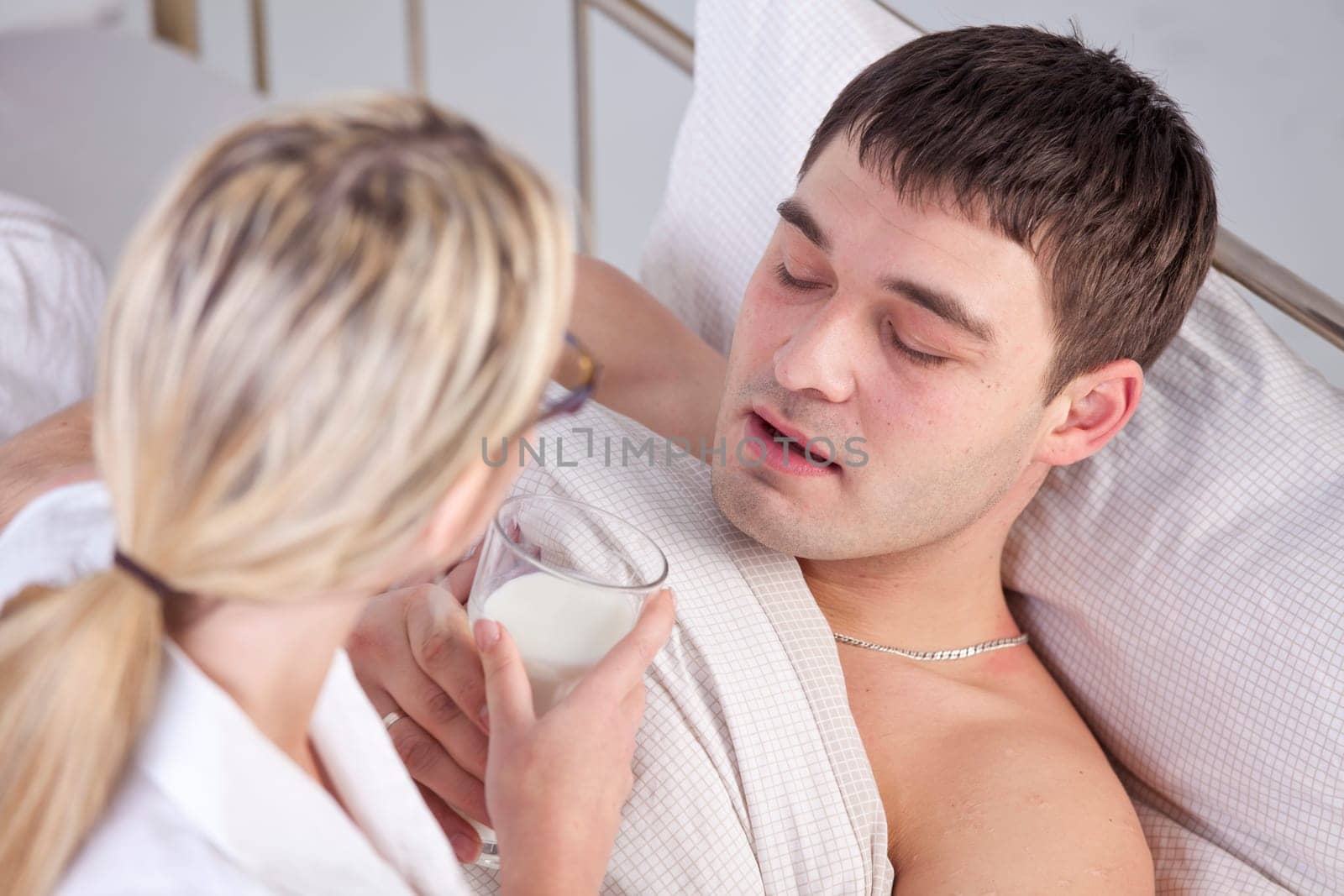 Sick man on bed drinking milk from female hands
