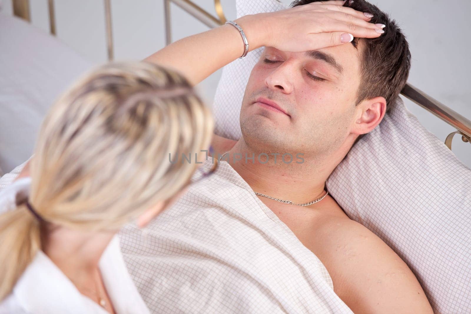 Sick man in bed, female doctor puts her hand on forehead