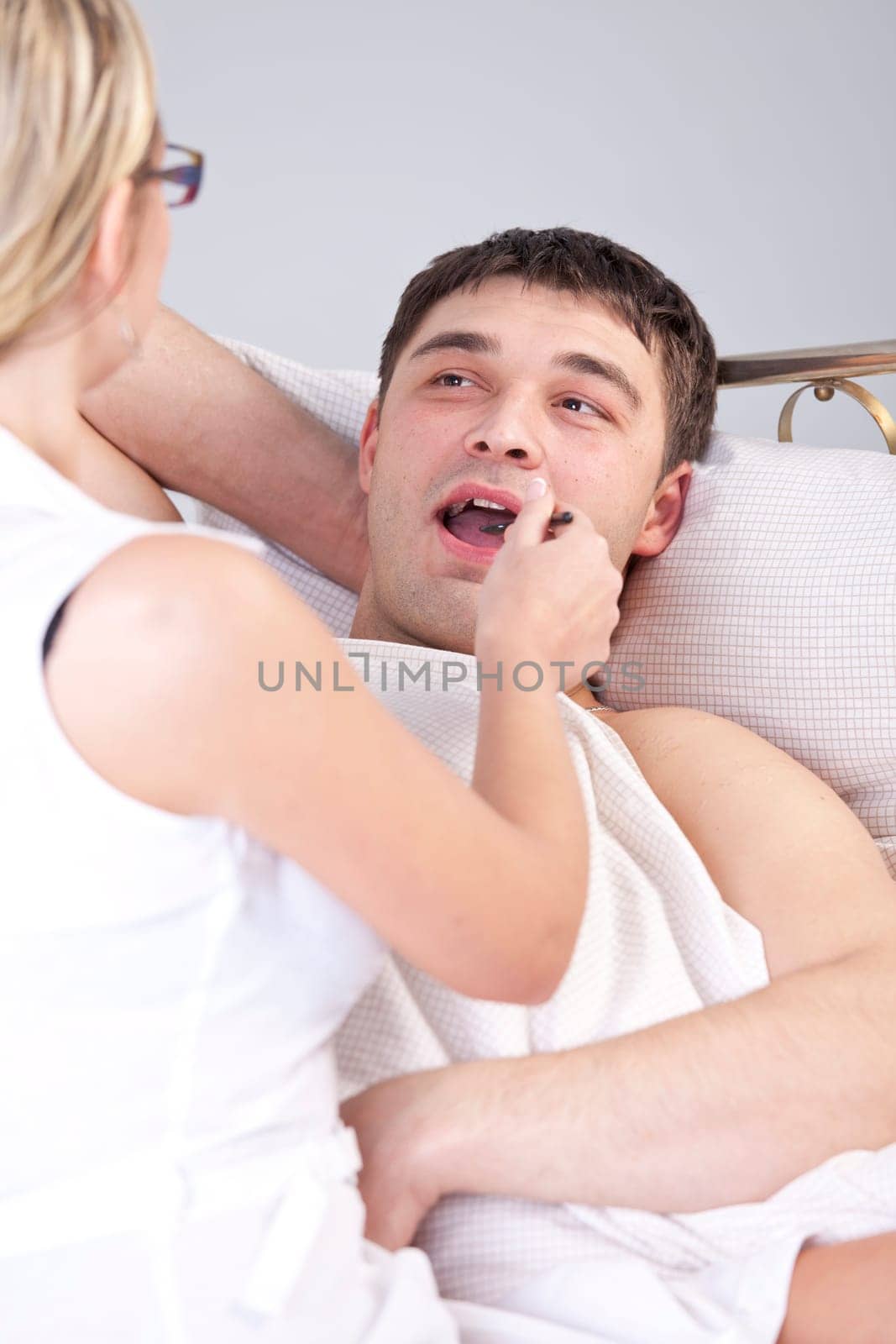 Female doctor examining male tongue on the bed
