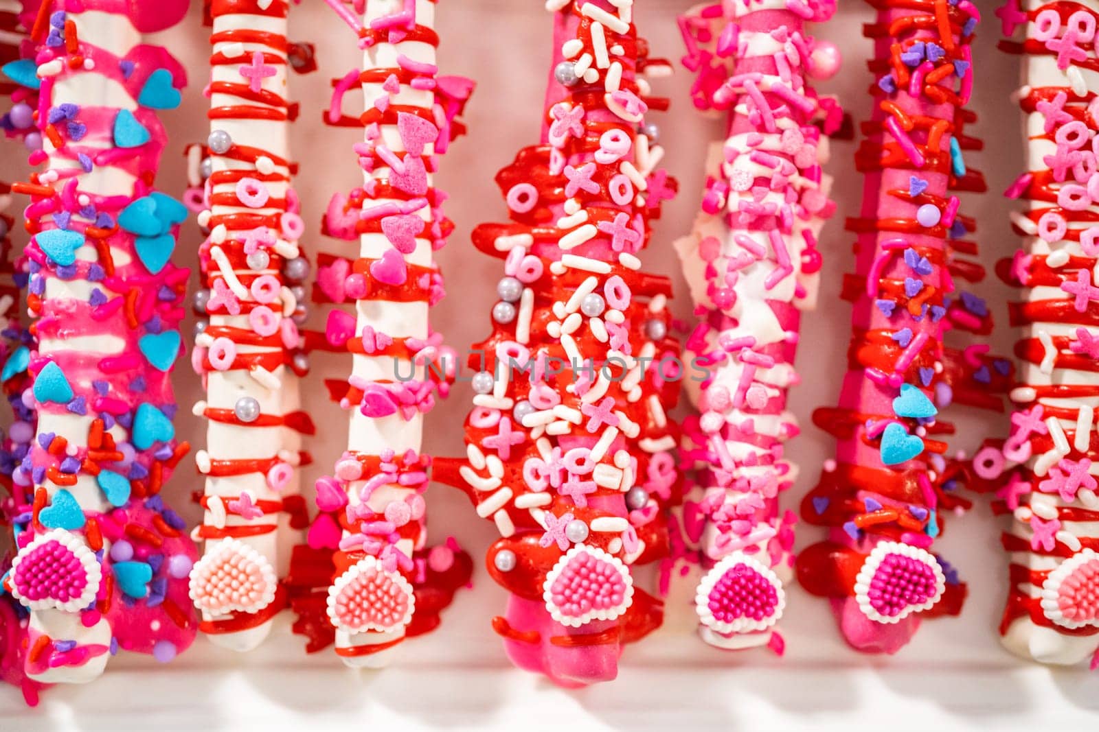 Chocolate-covered pretzel rods decorated with heart-shaped sprinkles for Valentine's Day.