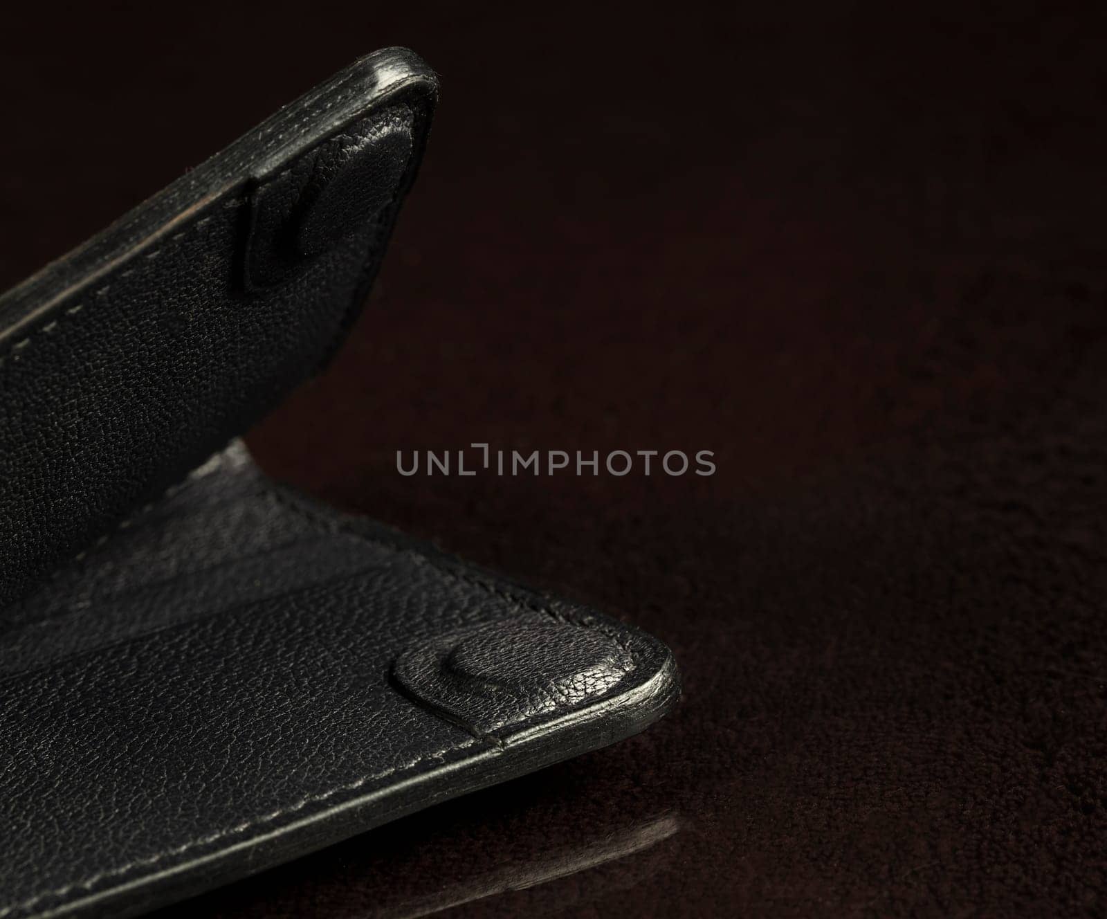 Part of a black leather wallet on a black background.