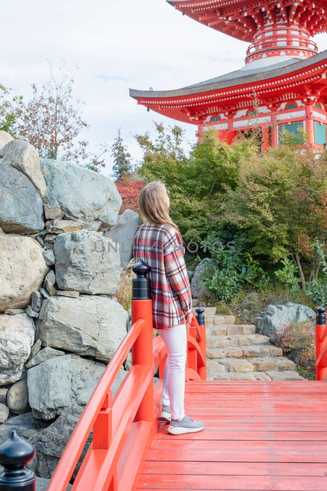 Woman in red plaid shirt enjoying nature walking in Japanese Garden with red pagoda