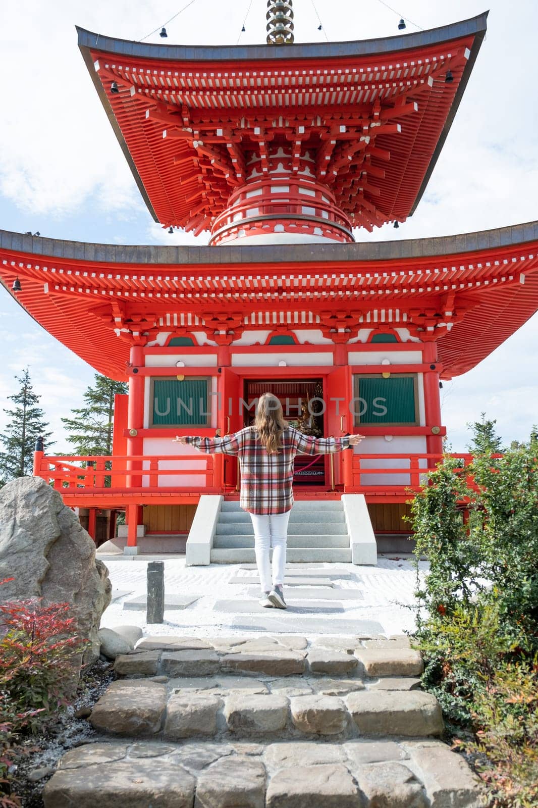 back view of unrecognizable Woman in red plaid shirt enjoying nature walking in Japanese Garden with red pagoda