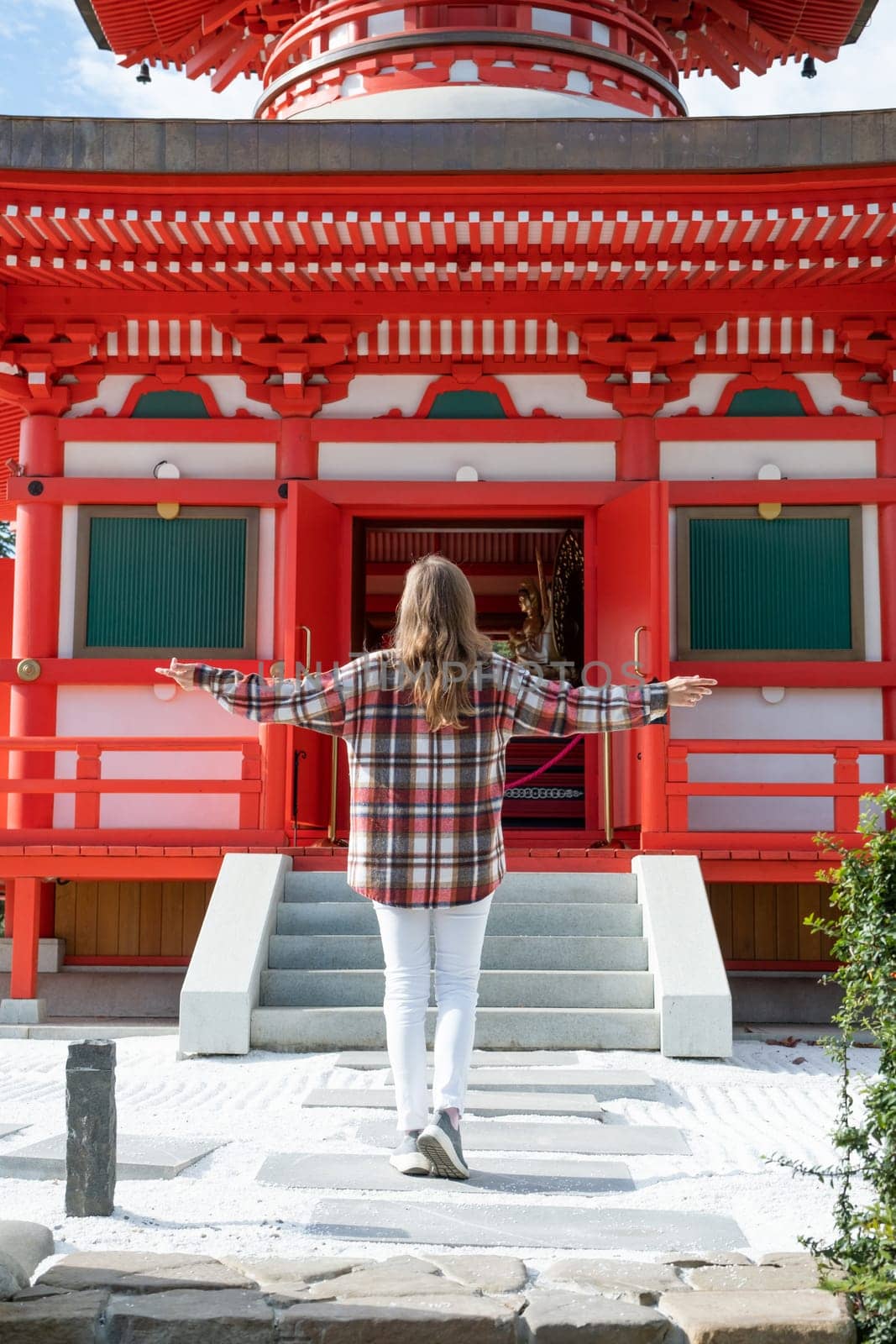 back view of unrecognizable Woman in red plaid shirt enjoying nature walking in Japanese Garden with red pagoda