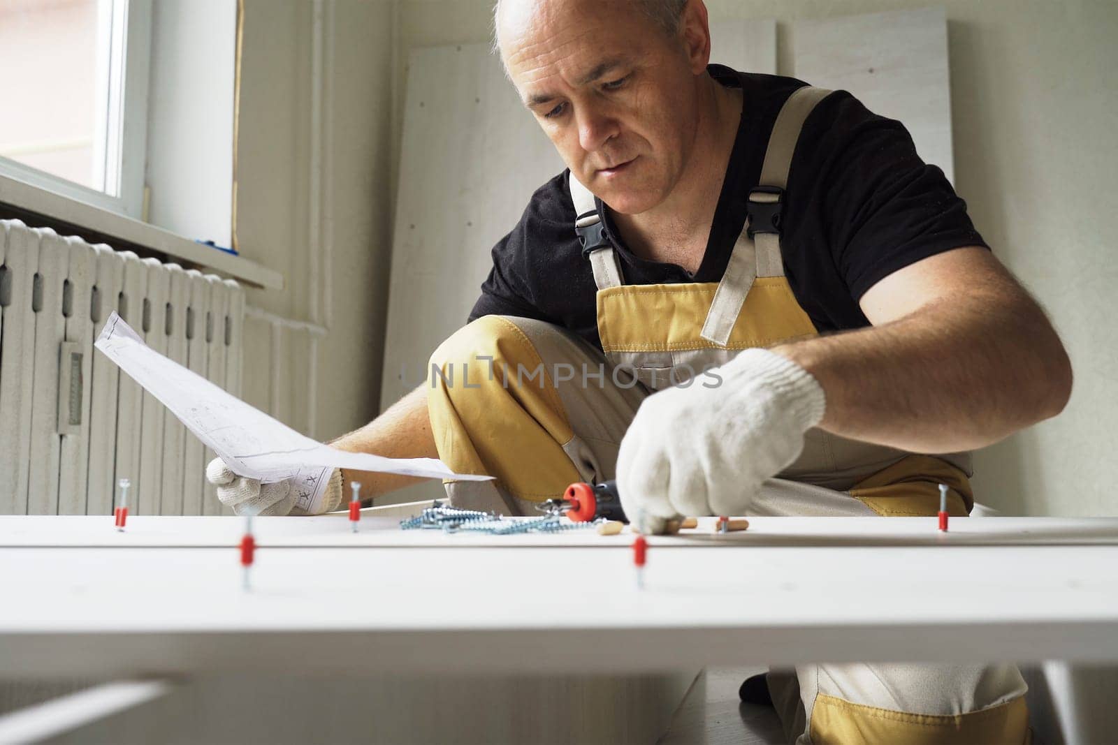 A male worker studies instructions before assembling furniture. Overall plan.