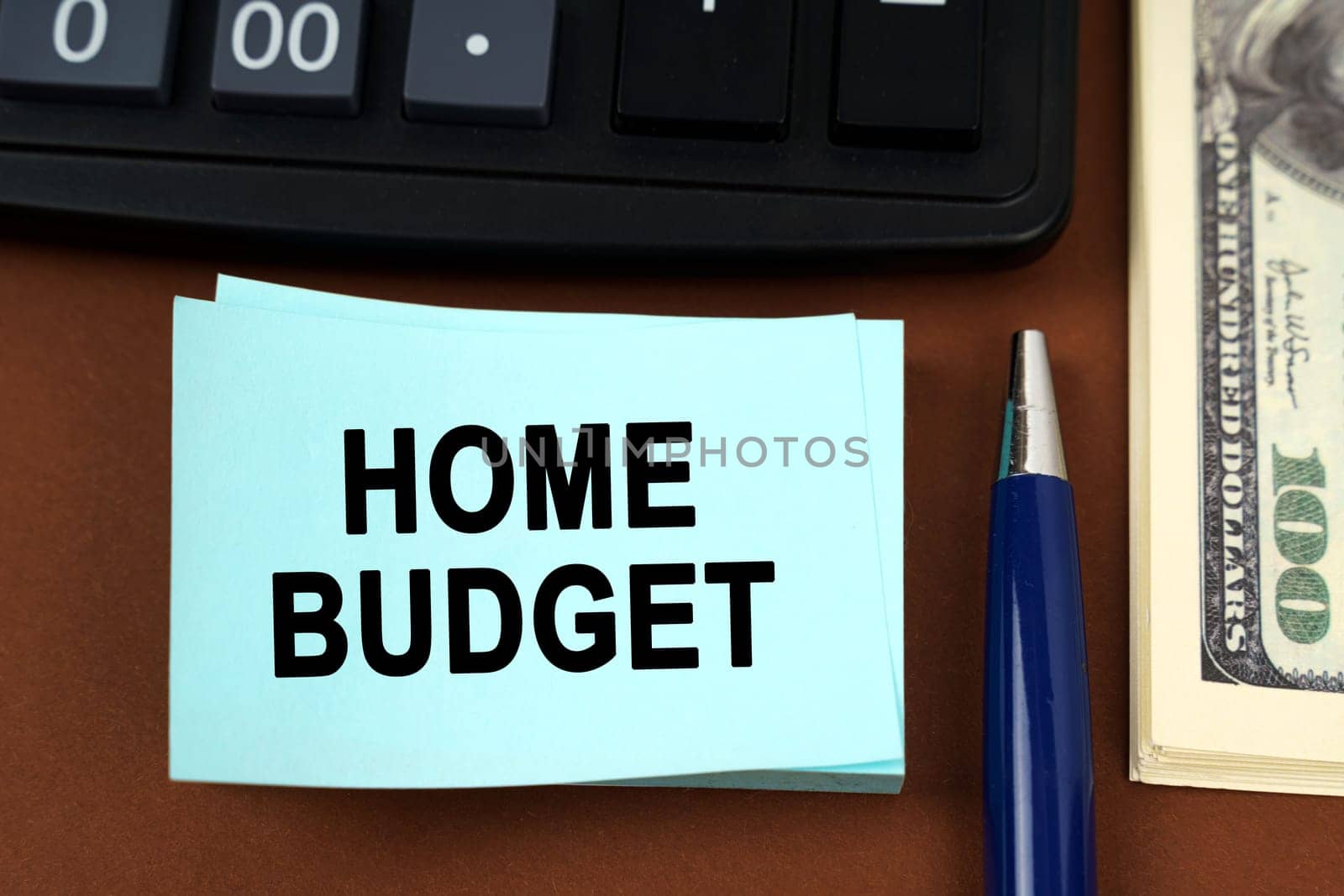 Business concept. On a brown surface lies a calculator, dollars, pens and stickers with the inscription - HOME BUDGET