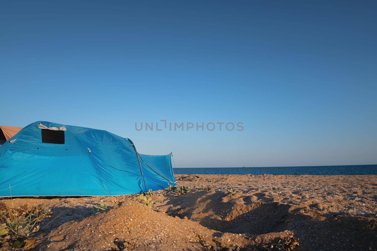 Tent, summer camping on the beach, against the backdrop of the sea and sky. A bright blue large tent stands on the sandy shore, no one by yanik88