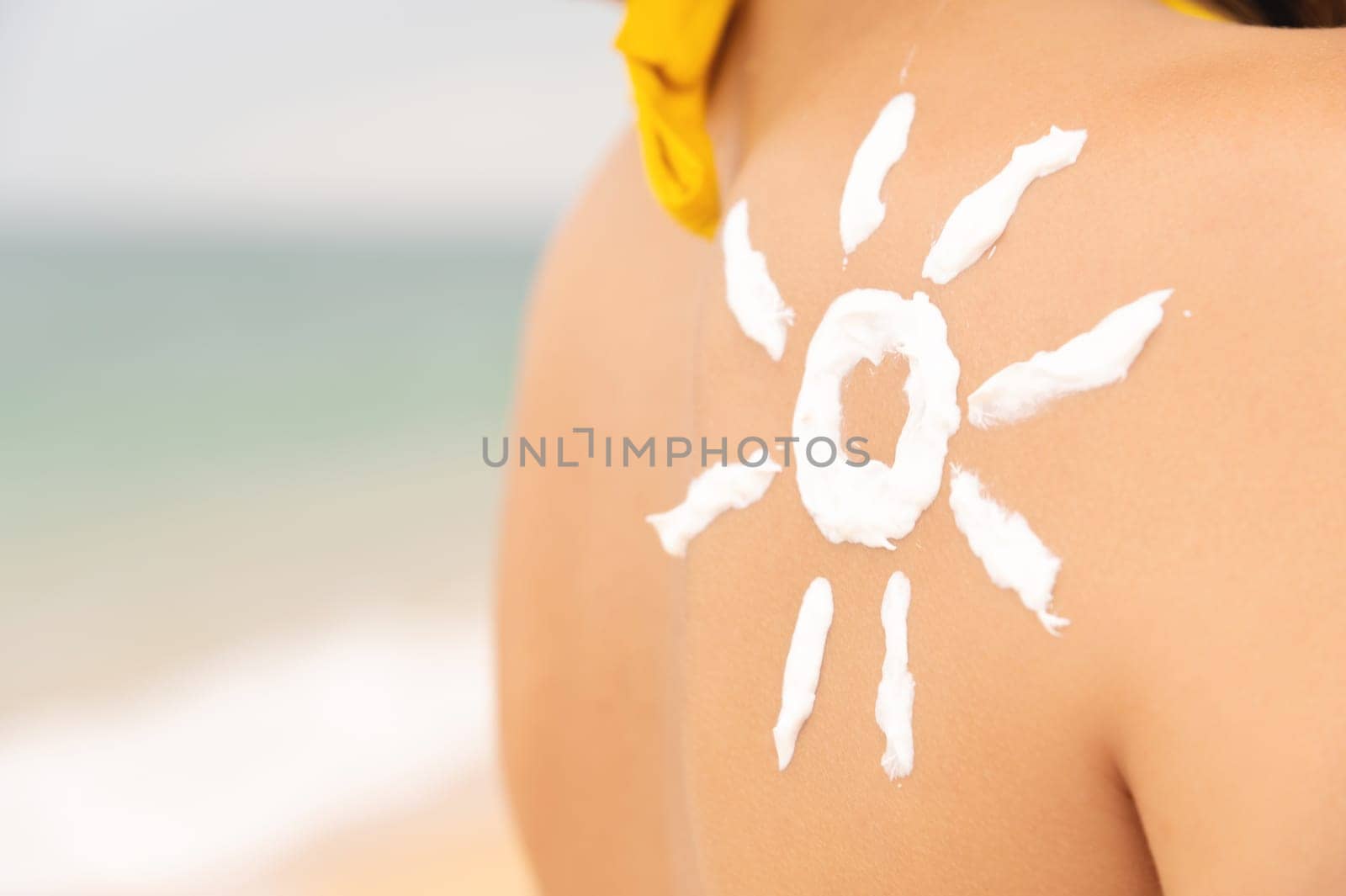 woman with sun-shaped suntan lotion on her shoulder, relaxing on the beach and taking care of her health. happy girl with the sun on her back by the sea in nature by yanik88