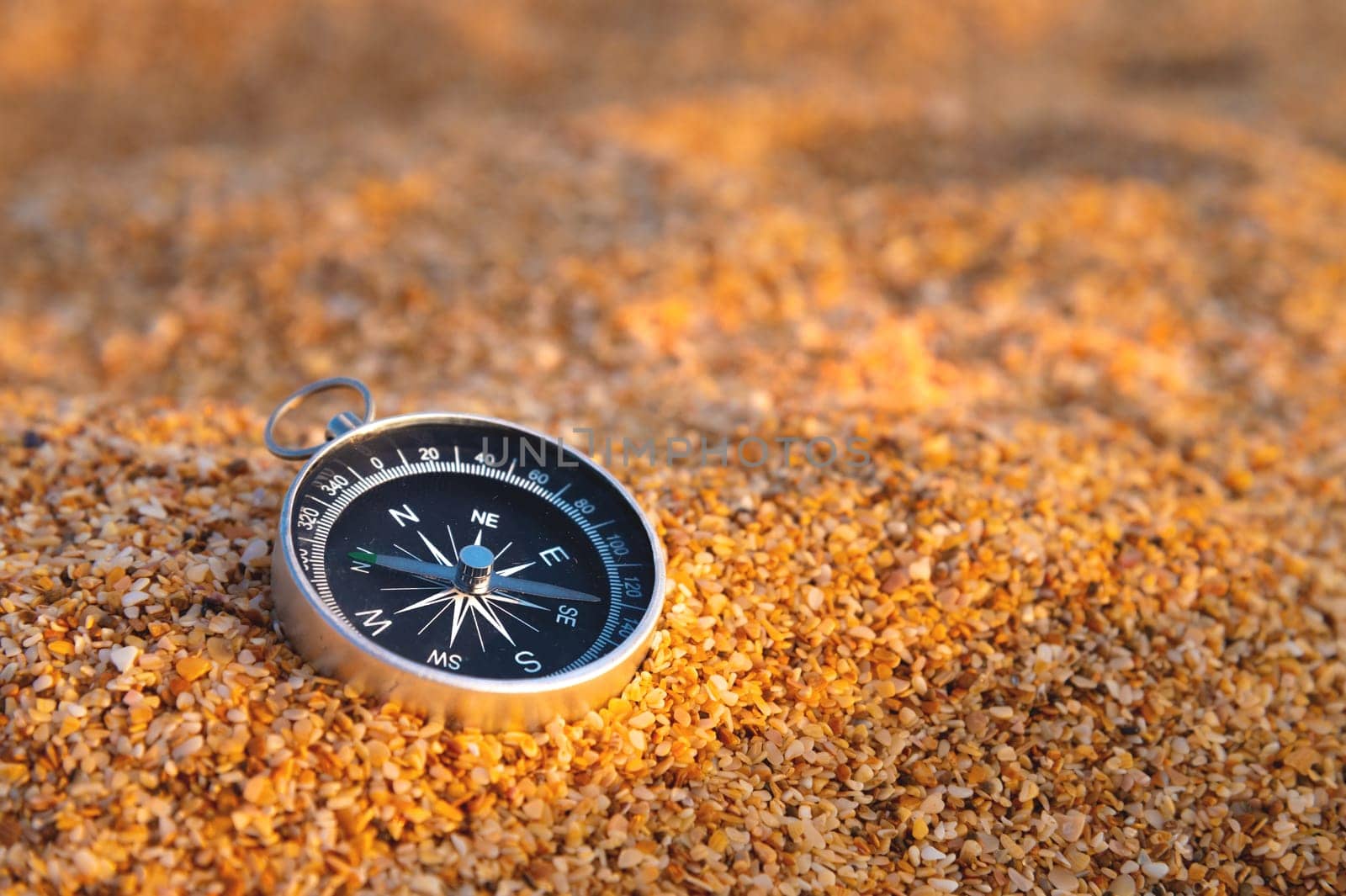 the compass lies on the golden sand, on the beach of shells on a sunny day.