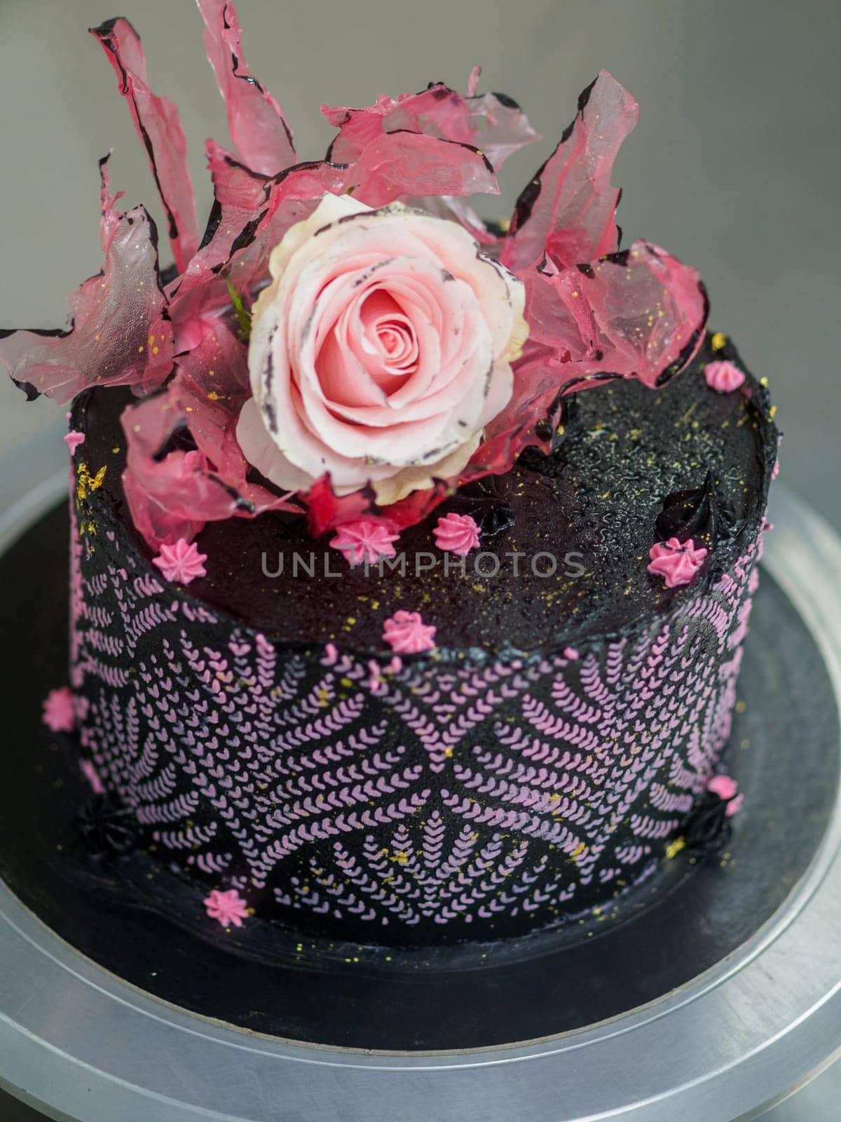 frosted icing black decorate cake for birthday celebration, real rose topping and pink sweet swirls in professional kitchen