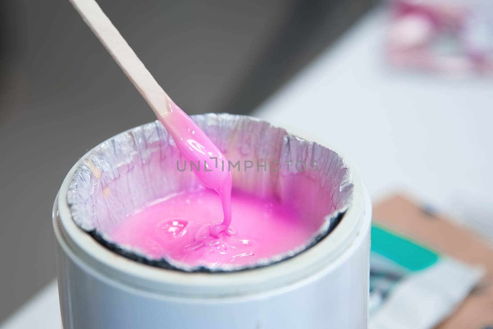 Close-up of a wax heater with hot pink wax and a wooden spatula. various cosmetics and tools on the table in a beauty salon.