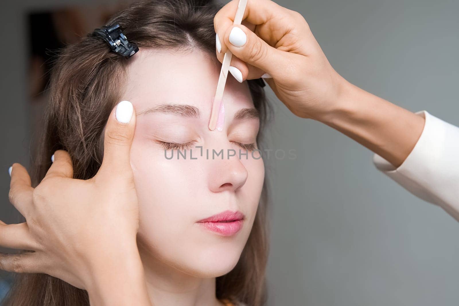 A cosmetologist removes hair from a beautiful woman's face with hot wax. A woman undergoes a cosmetic procedure. Epilation removing hair from the face, skin care and health concepts. by yanik88