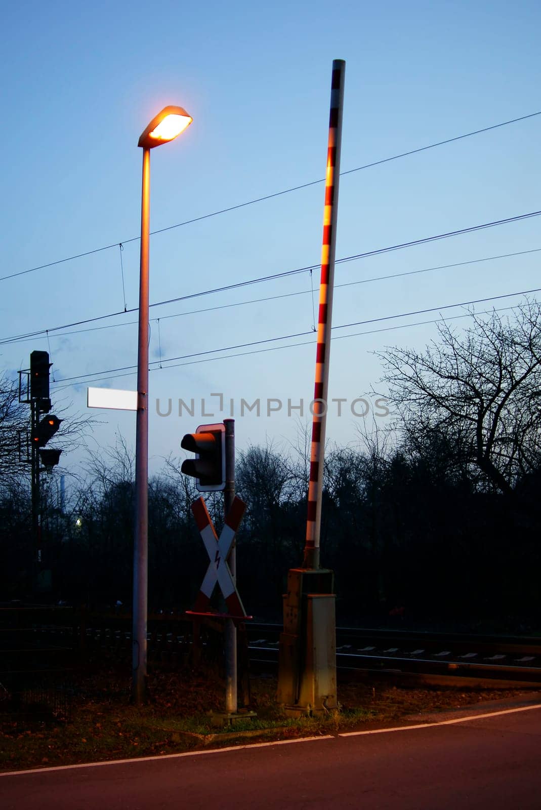 The photograph of a level crossing with an open barrier and a lantern in the evening.