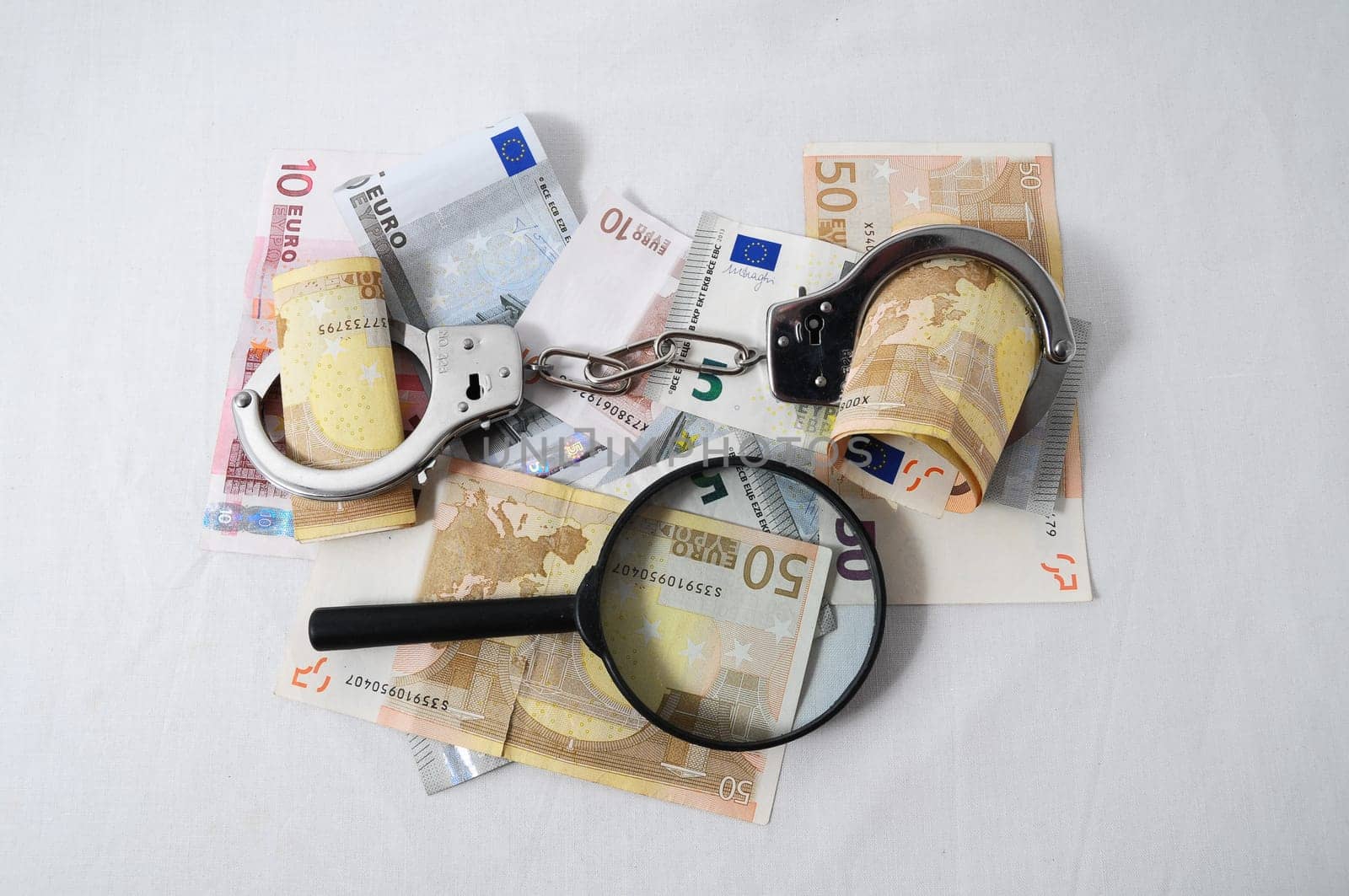 Financial Concept Loupe, Handcuffs and Money on a White Background