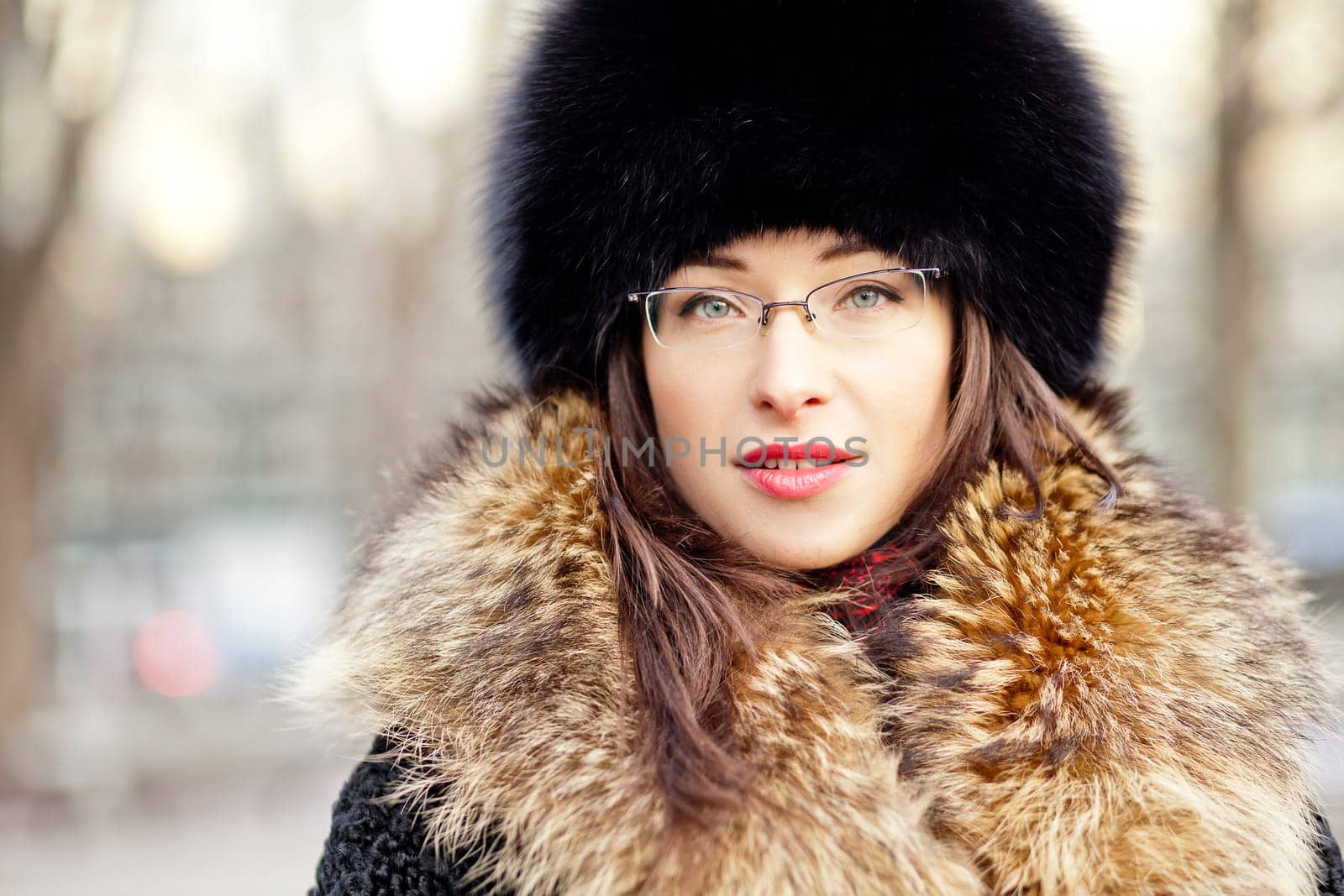 Winter style girl wearing fur hat and glasses in the city park