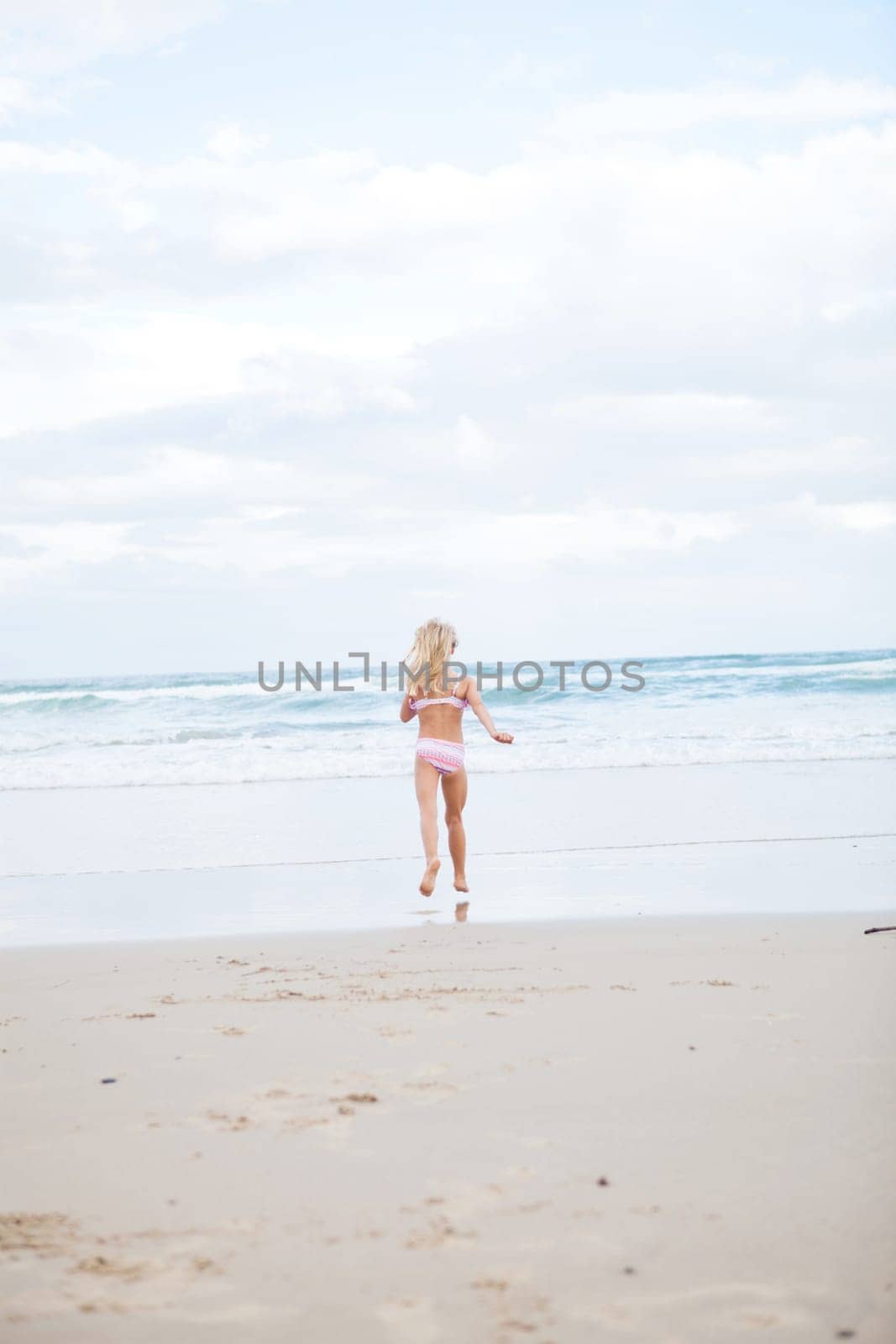 Young girl in swimming suit running towards water at beach