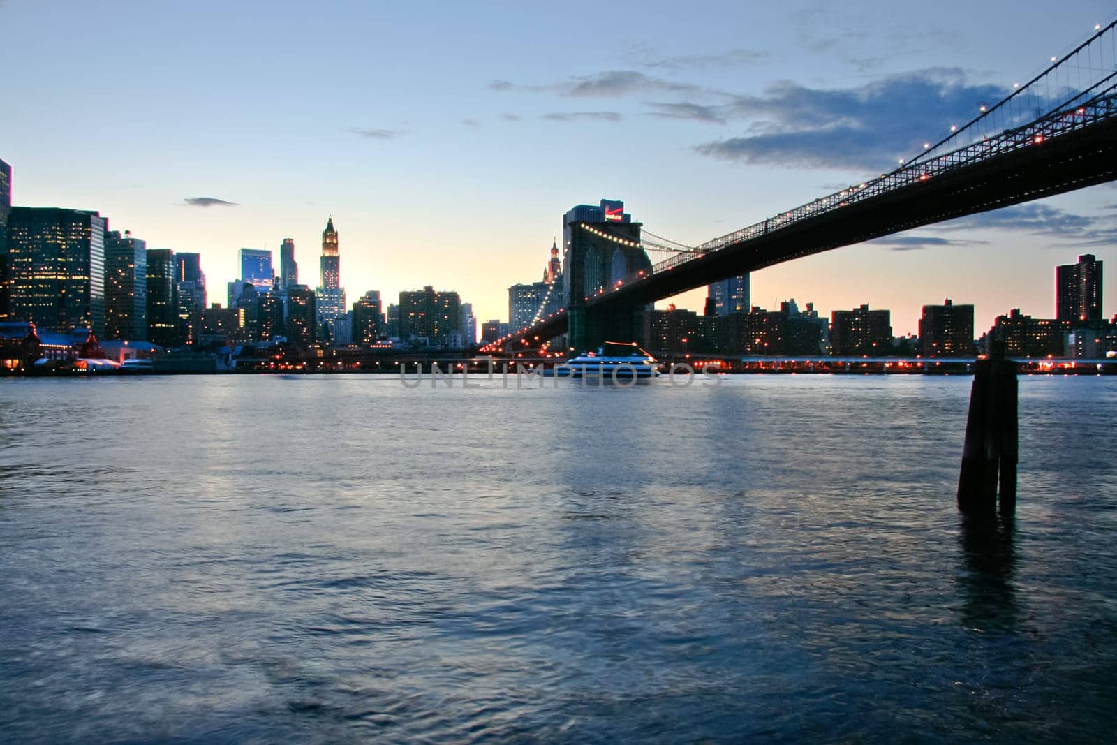 New York City Manhattan skyline panorama with Brooklyn Bridge and office skyscrapers building in at dusk illuminated with lights at night