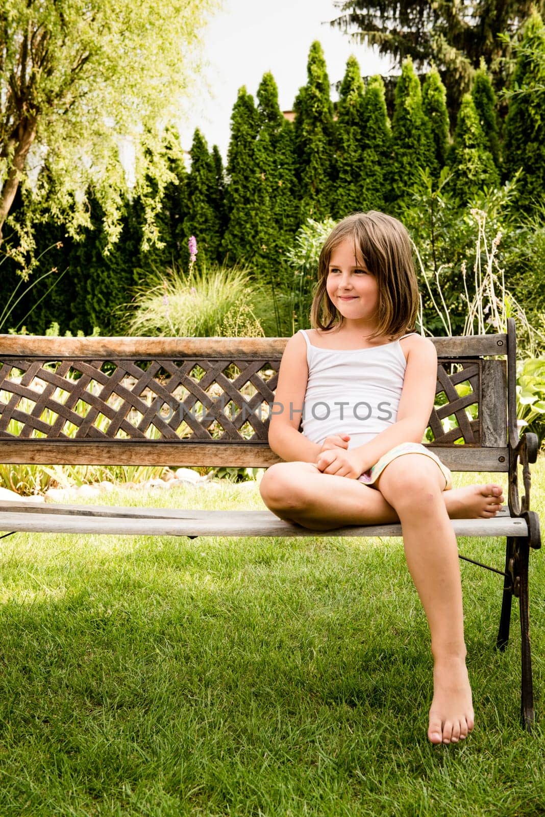 Daydreaming child portrait - little girl sitting on bench outdoor in backyard