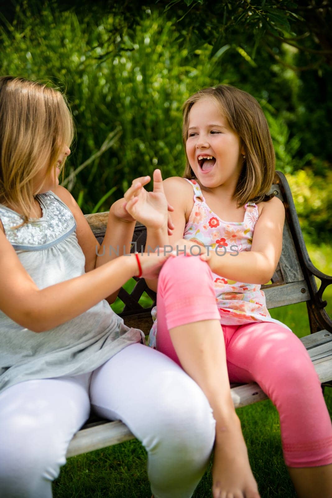 Two small girls (sisters) larking in backyard sitting on bench