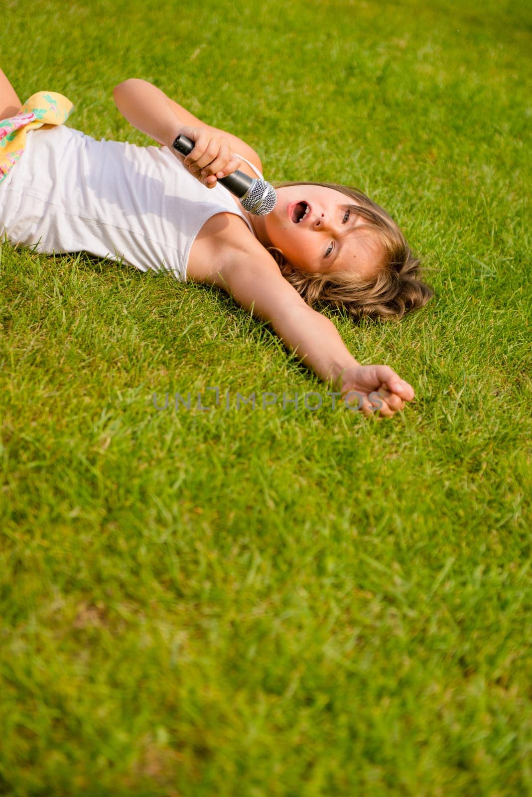 Child singing with microphone and lying on grass - outdoor lifestyle