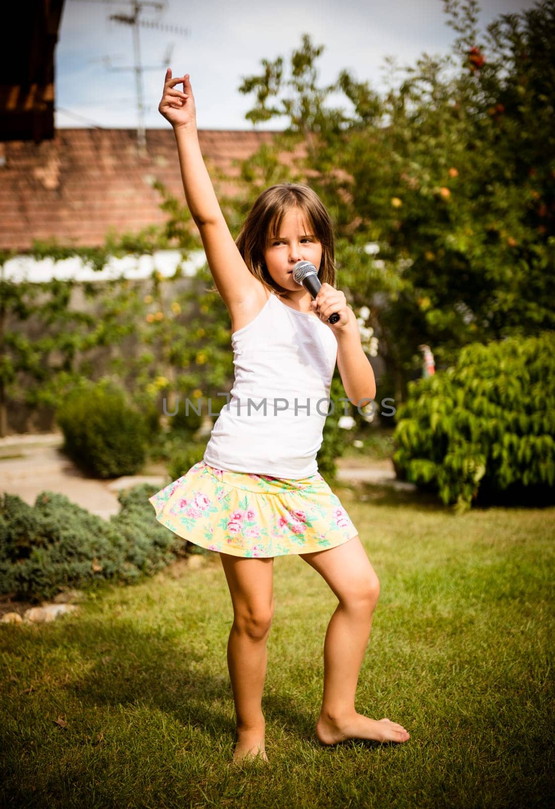 Happy childhood - child singing with microphone outdoor in backyard