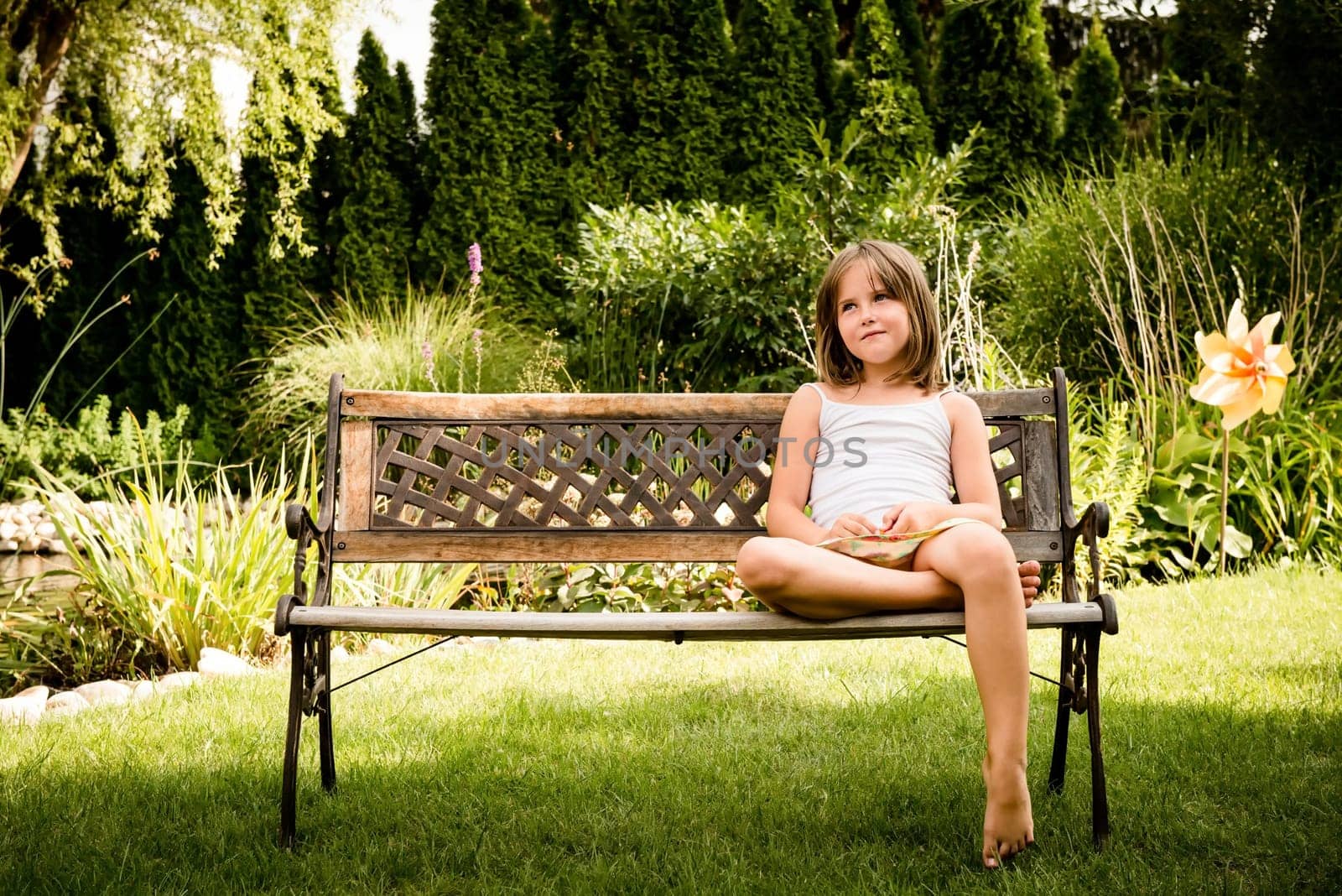Daydreaming child portrait - little girl sitting on bench outdoor in backyard
