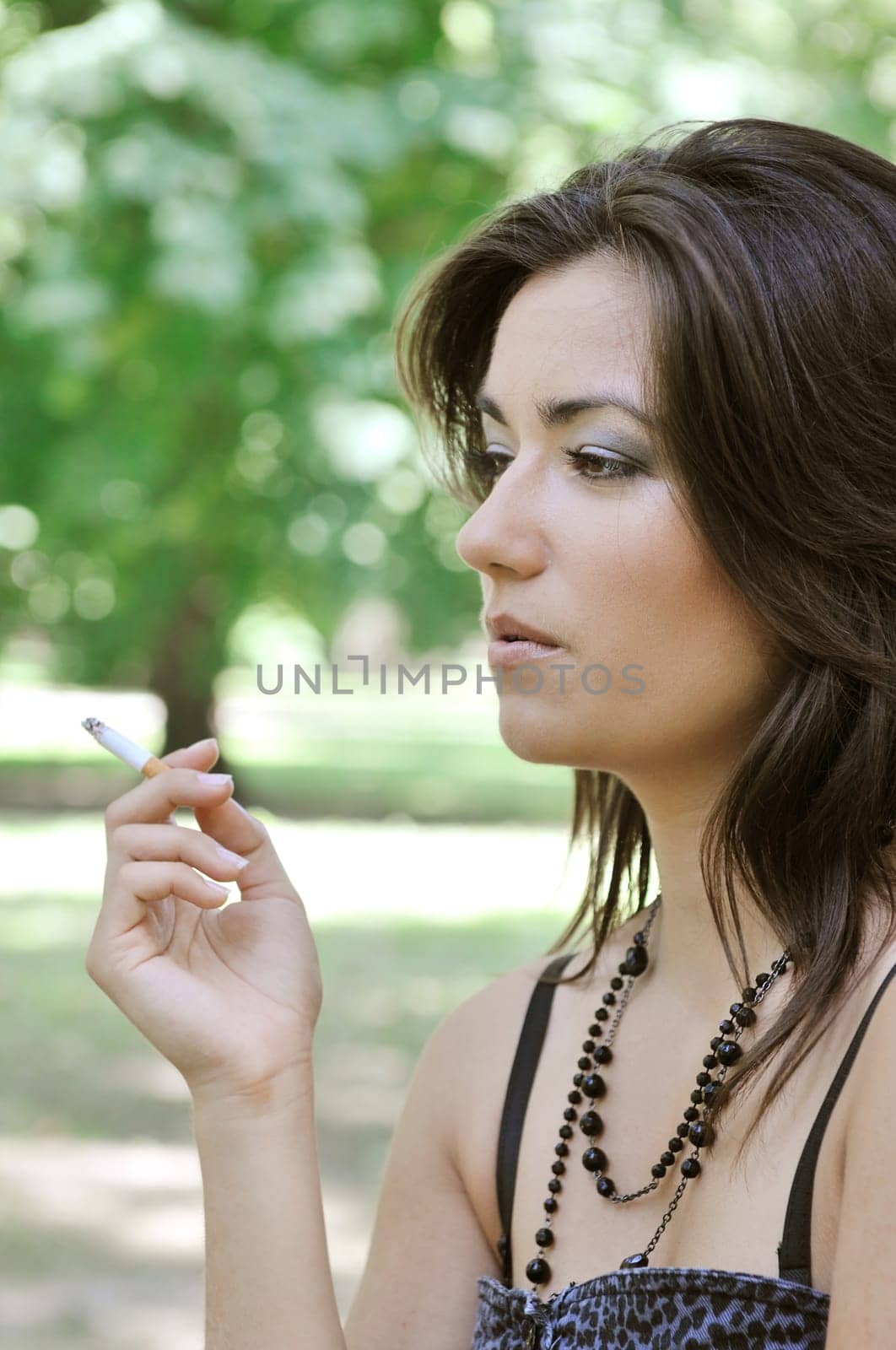 Portrait of young woman smoking cigarette outdoors in sunny green park