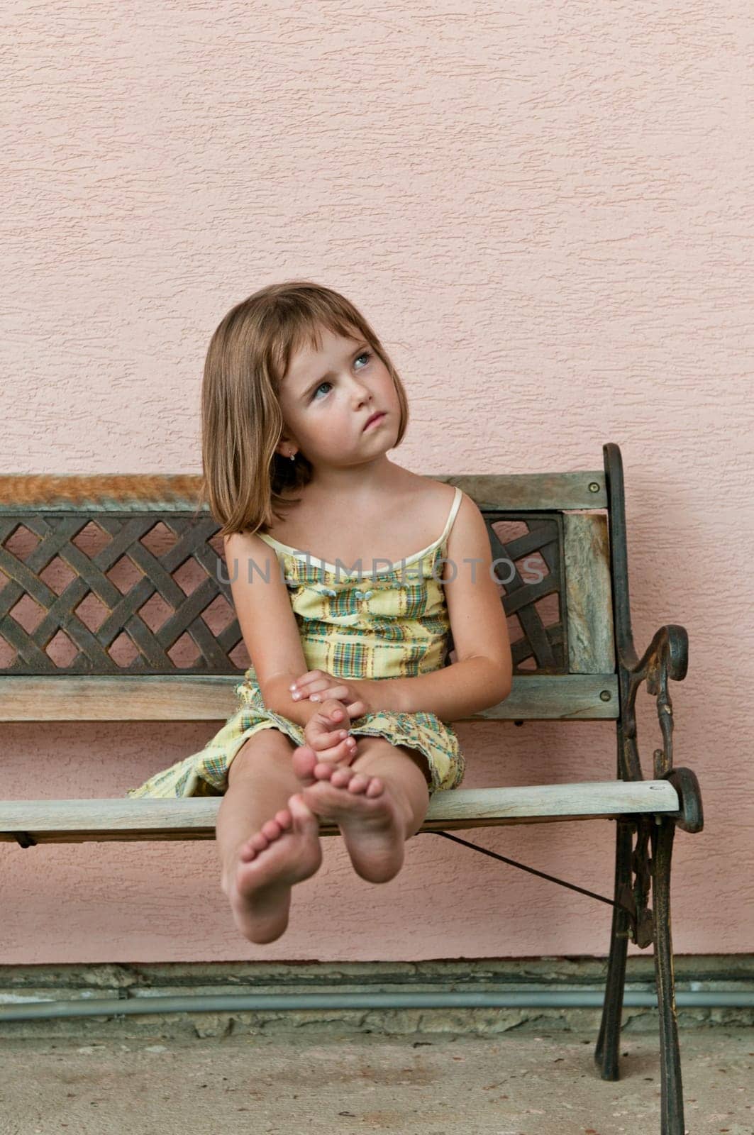 Portrait of cute child sitting on bench and stretching barefoot legs
